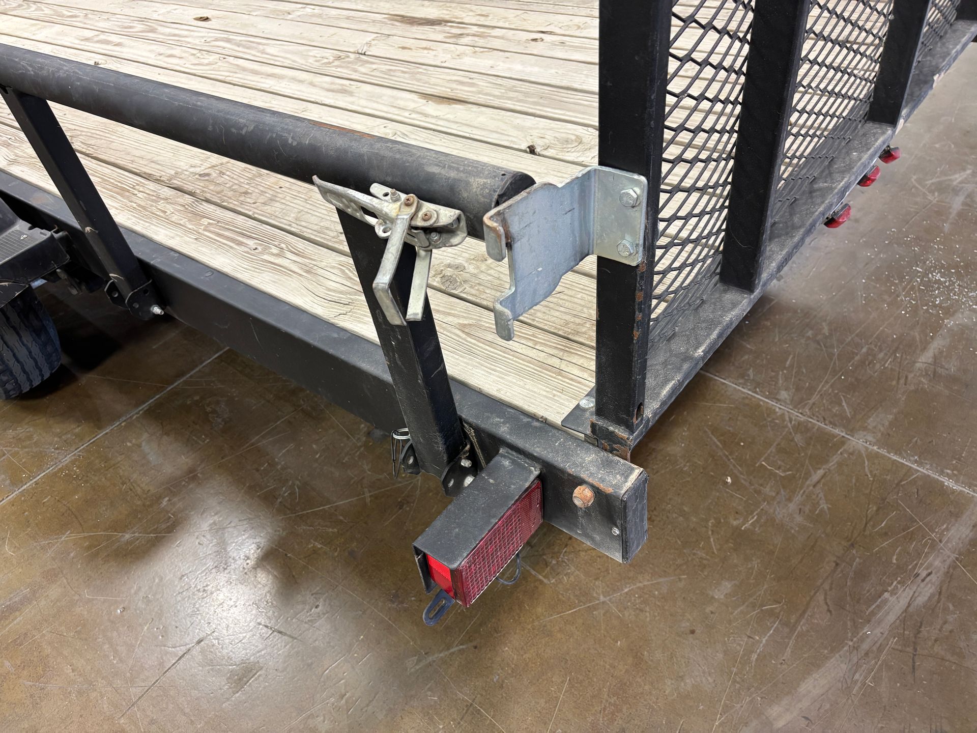 Black trailer with wooden deck and mesh sides, latch detail.