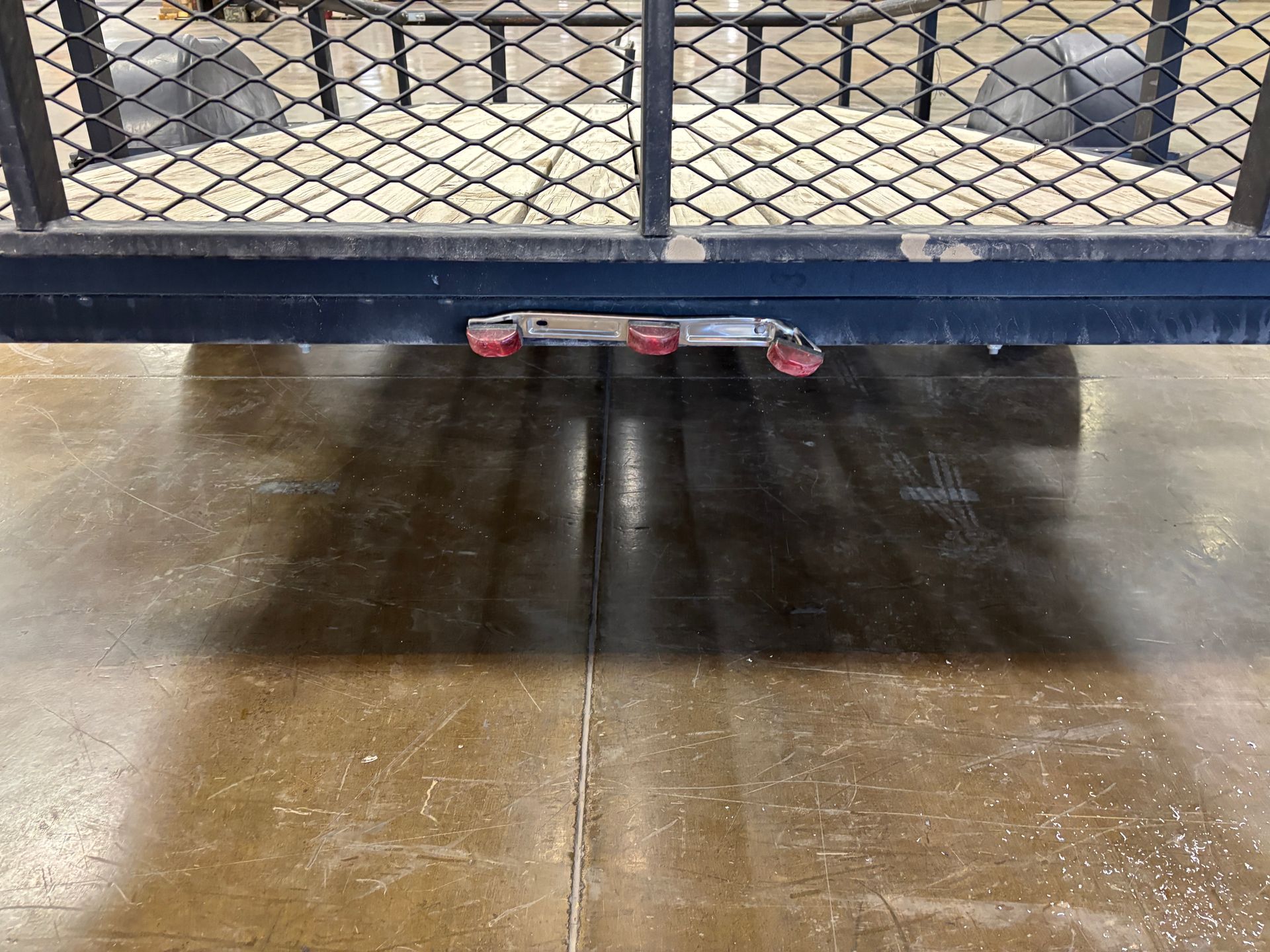 Black trailer hitch with red lights, seen from below on a concrete surface.