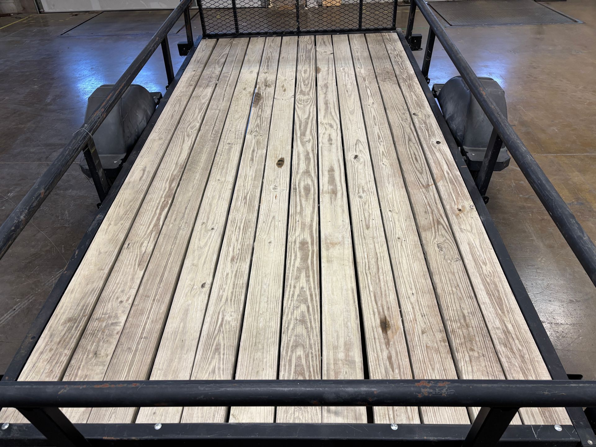 Flatbed trailer with weathered wooden planks. Black metal frame and railing.