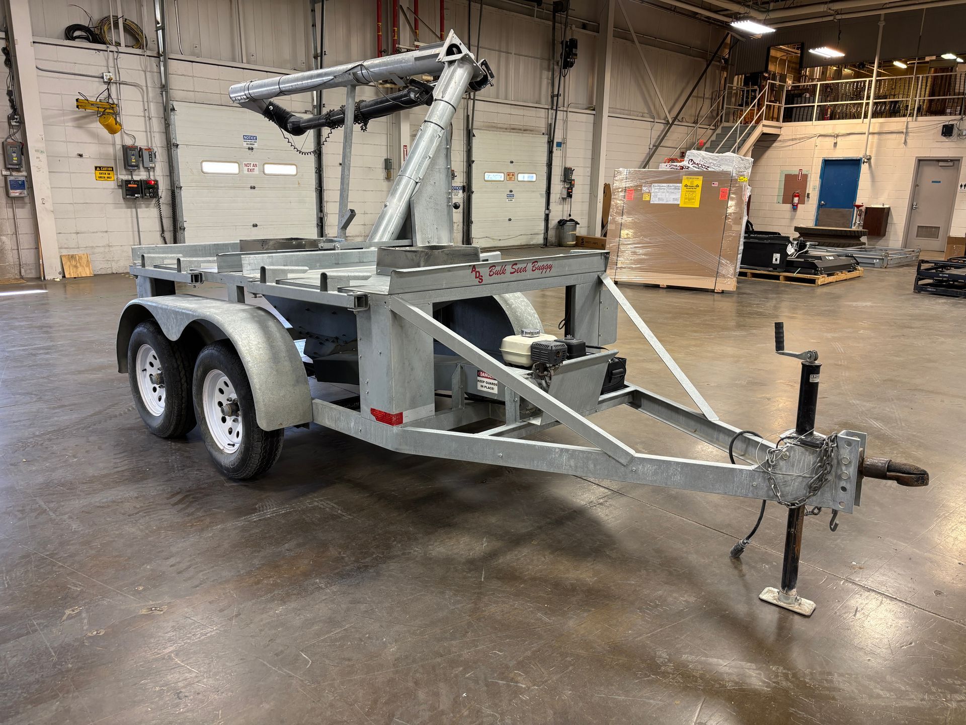 Gray utility trailer with two wheels, in an industrial setting.