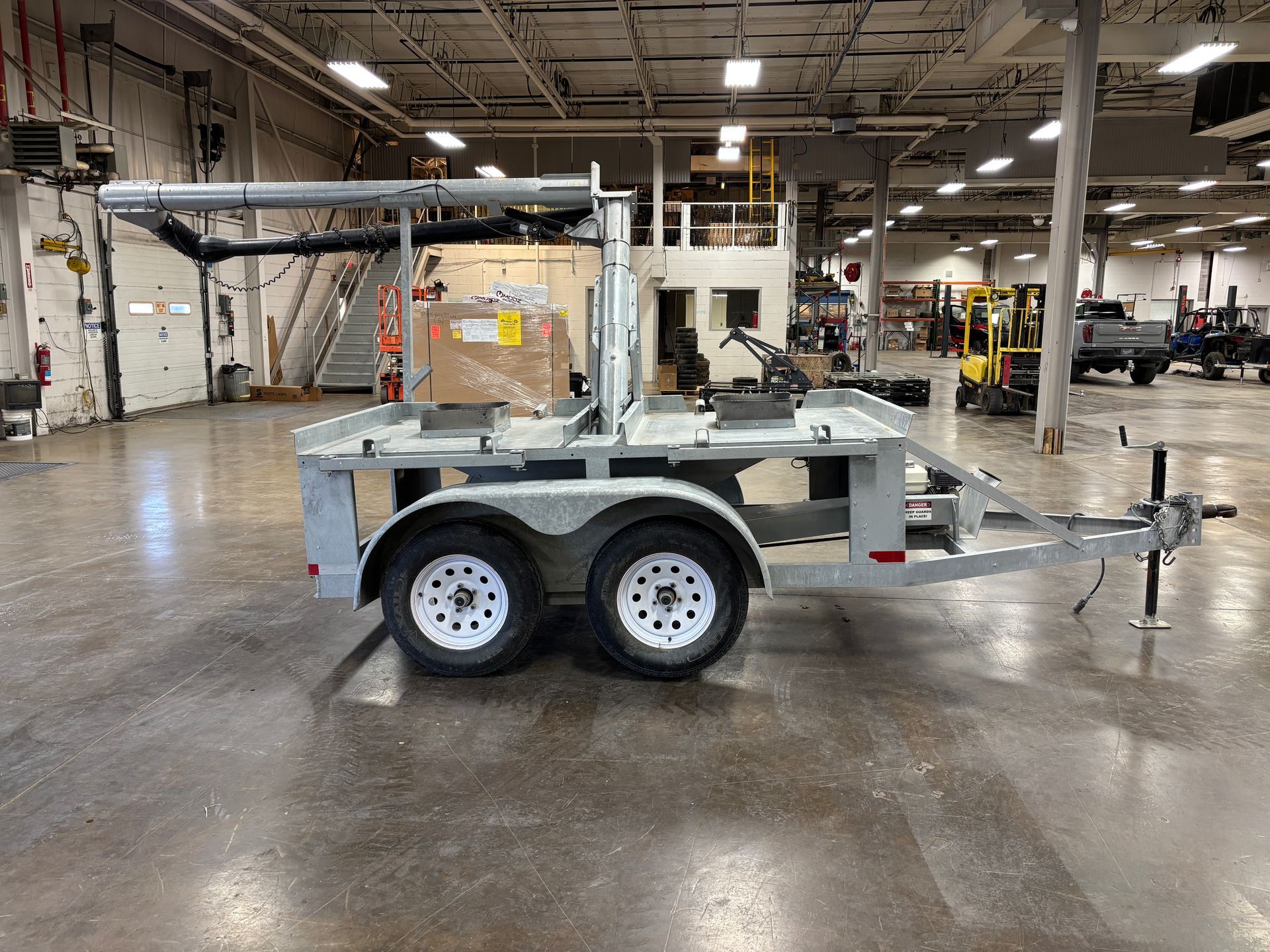 A utility trailer with dual wheels, equipped with metal racks in an industrial setting.
