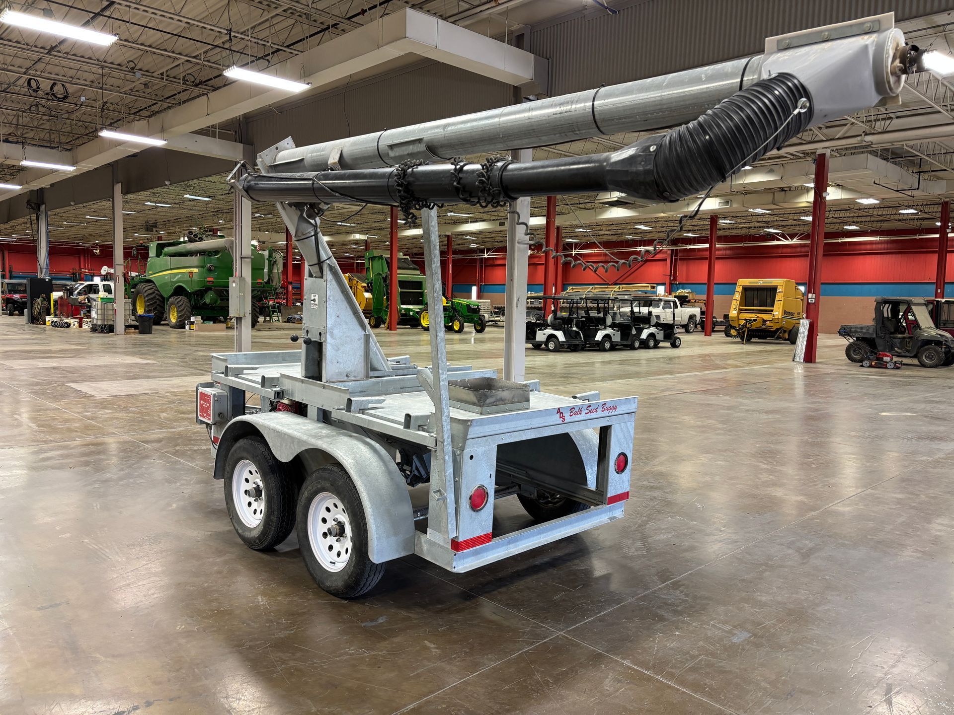 Gray trailer with a long, curved tube; inside a large building with farm equipment.