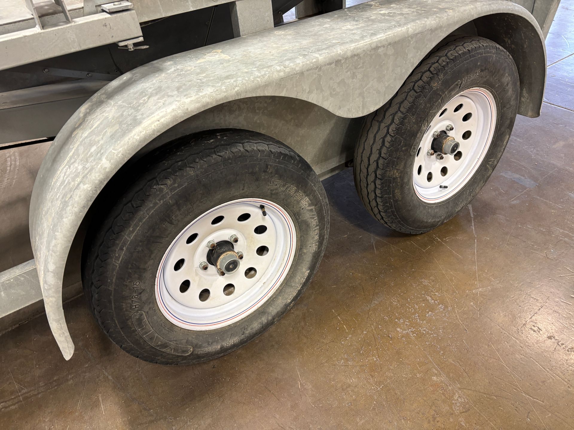 Two trailer tires with white rims and a gray fender.
