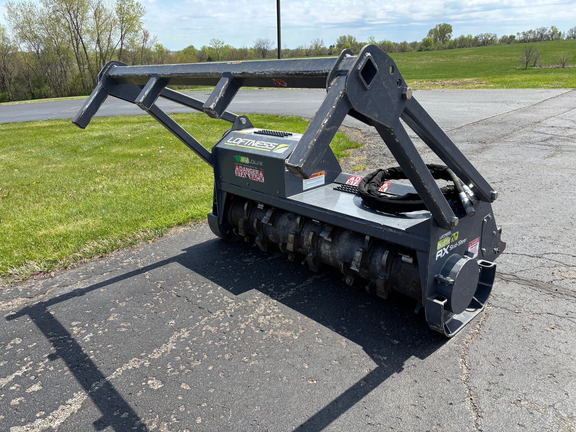 Gray Loftness mulcher on asphalt, with safety bar, on a sunny day.