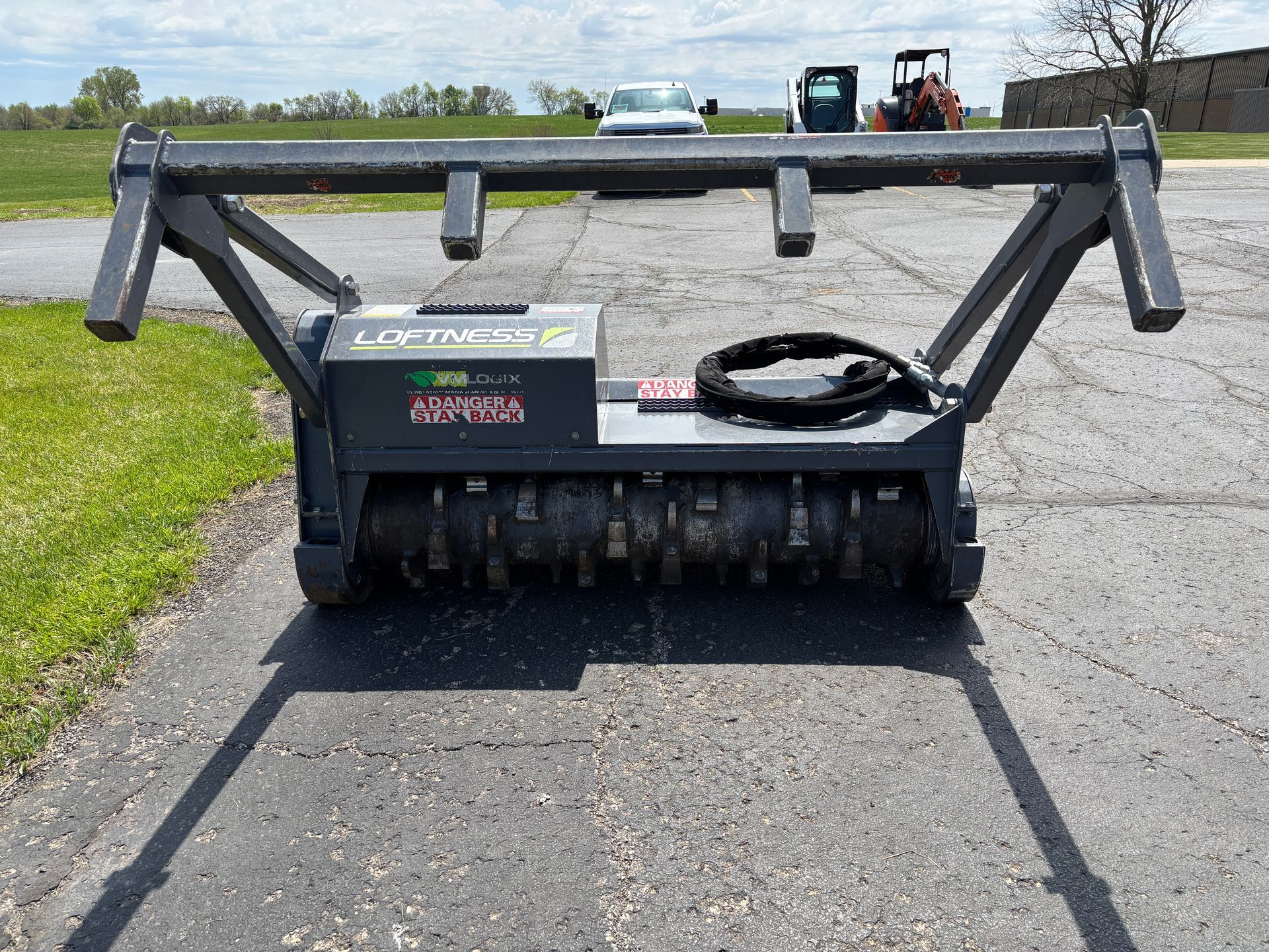 Gray Loftness mulcher on asphalt, with safety bar, on a sunny day, front shot.