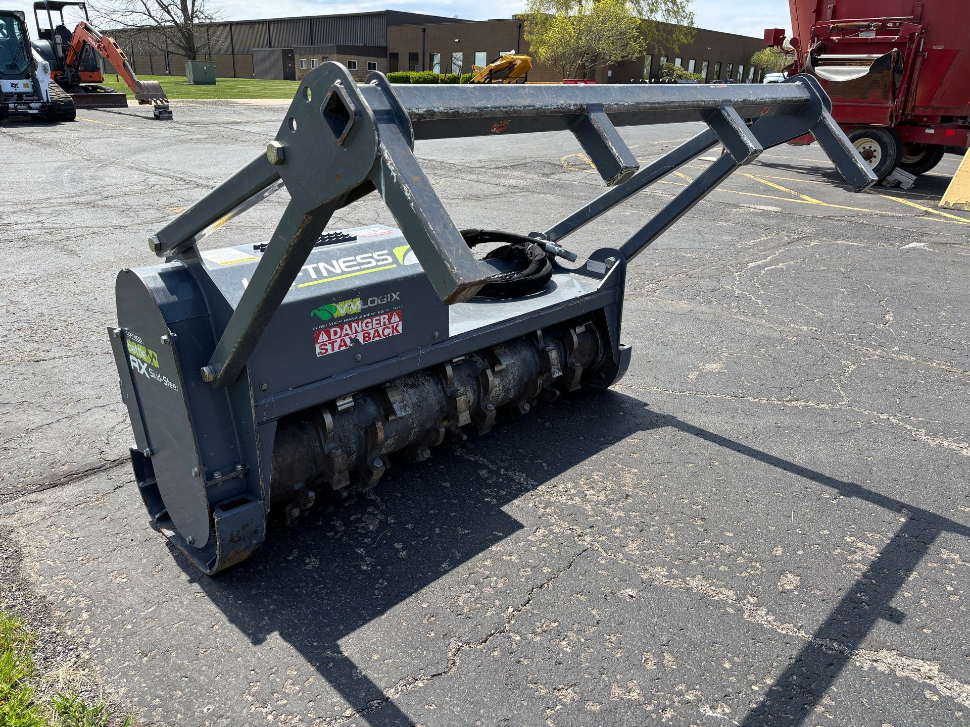 Gray Loftness mulcher on asphalt, with safety bar, on a sunny day.