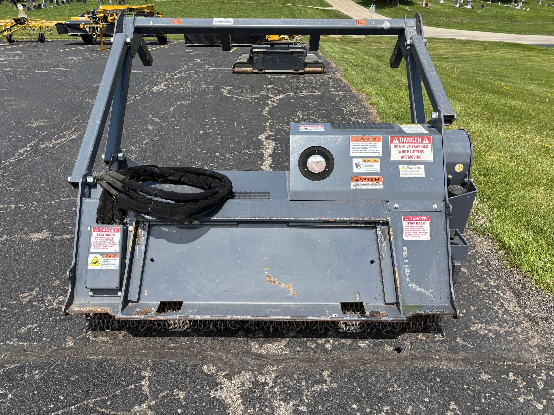 Gray Loftness mulcher on asphalt, with safety bar, on a sunny day, back shot.