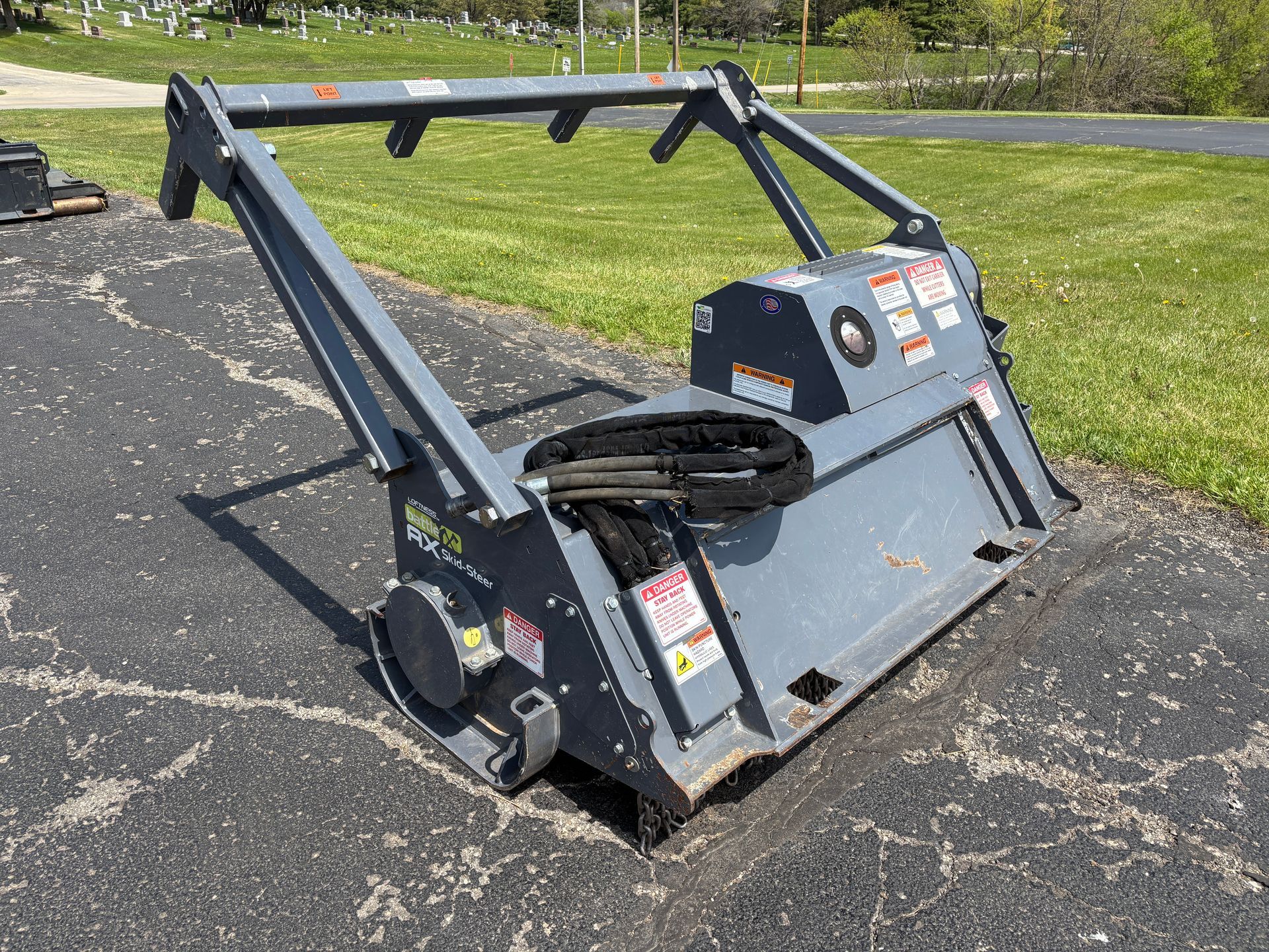Gray Loftness mulcher on asphalt, with safety bar, on a sunny day, back angle shot.