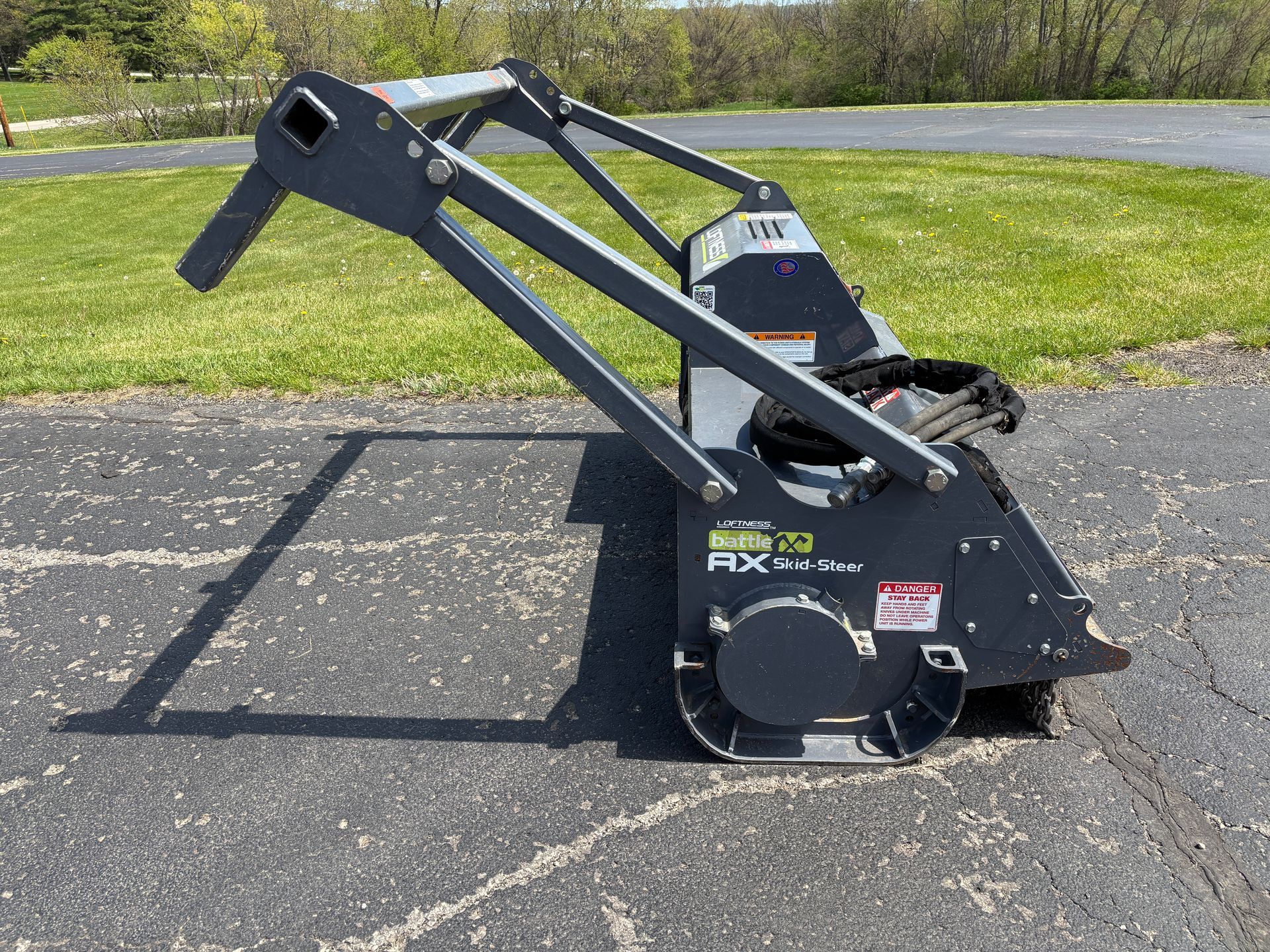 Gray Loftness mulcher on asphalt, with safety bar, on a sunny day, side view shot.