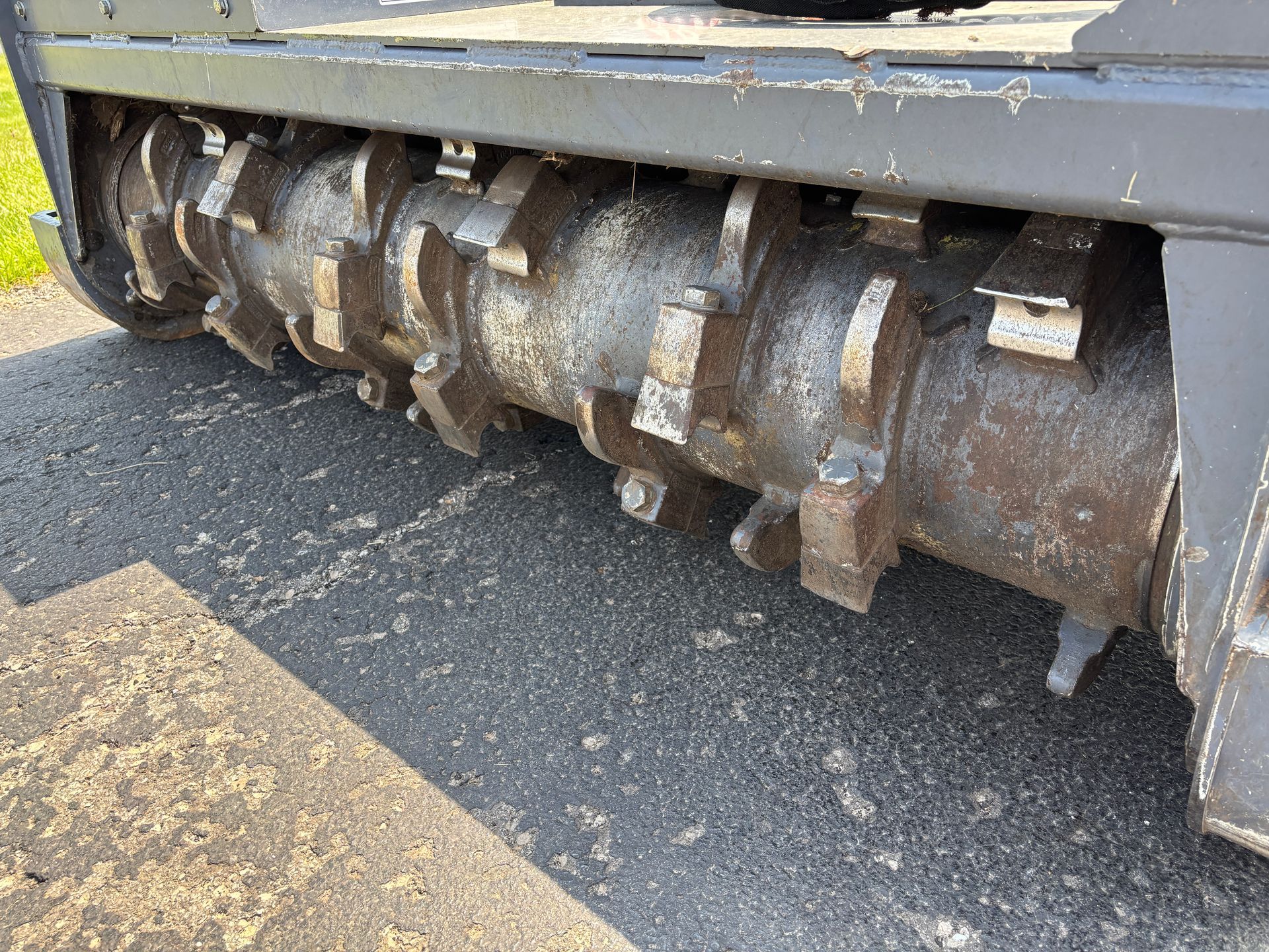Close-up of a heavy-duty mulcher's rotating drum with metal teeth.
