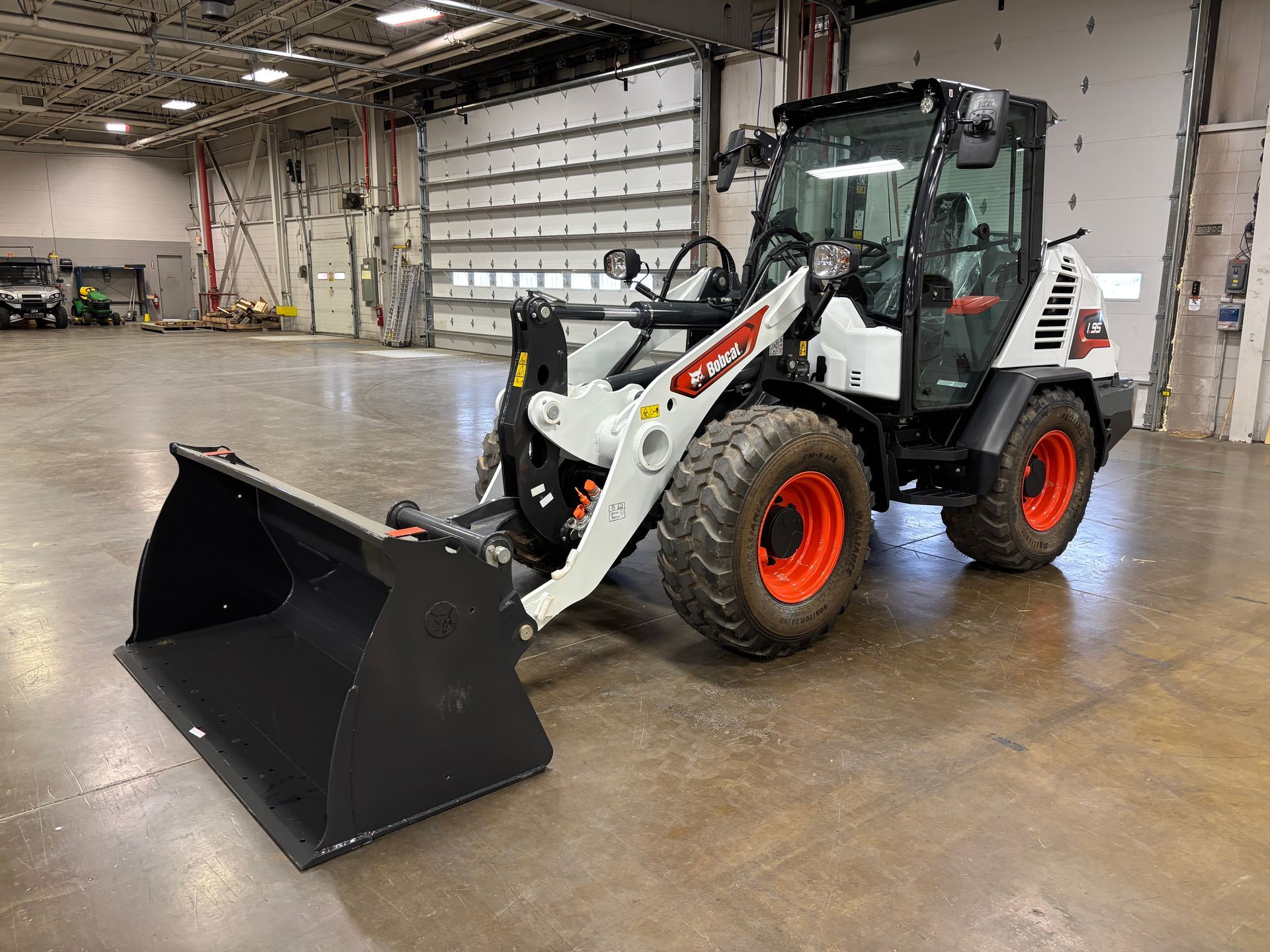 Bobcat compact wheel loader with bucket in a warehouse, white body, orange wheels.
