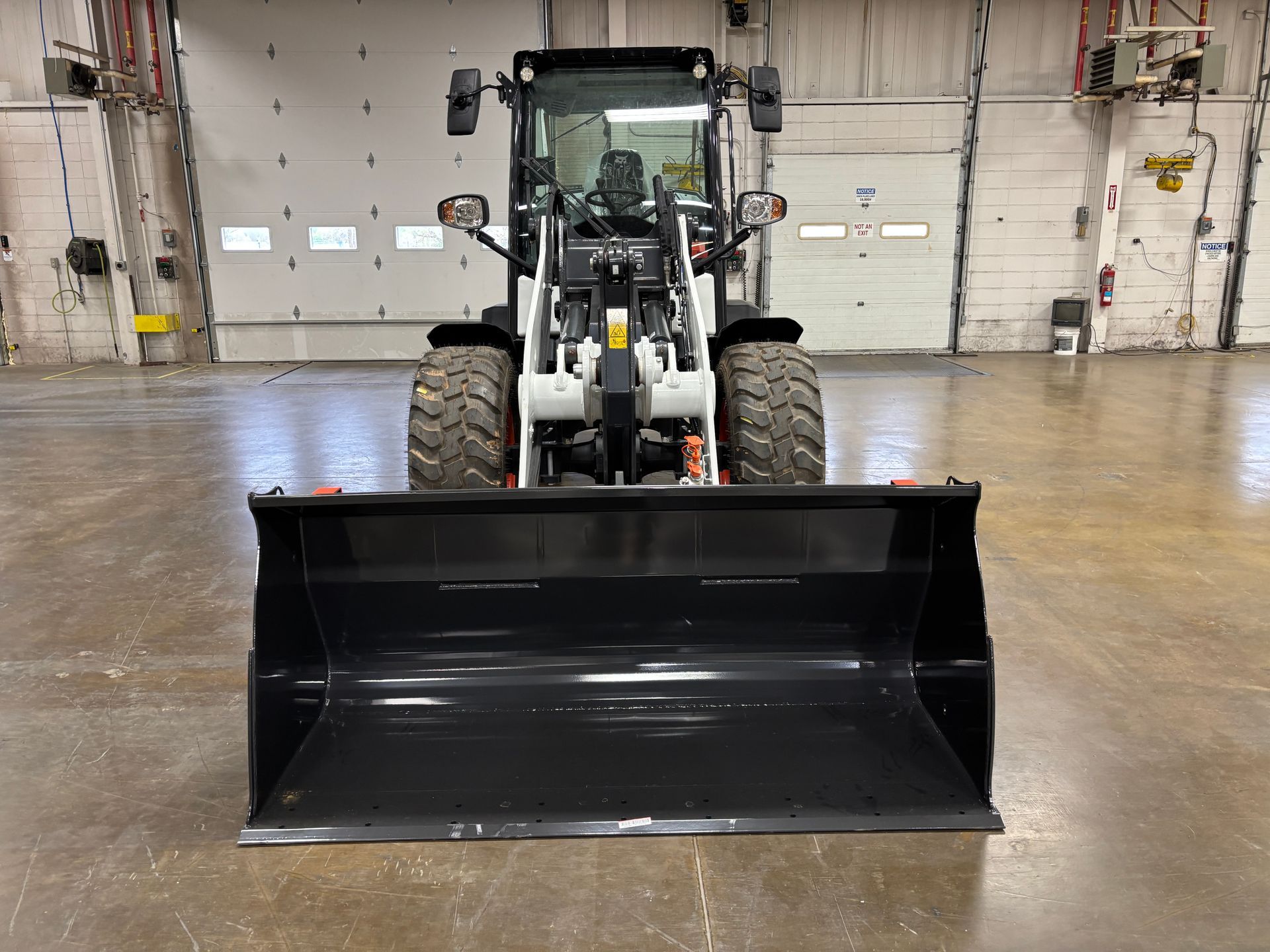 Front view of a black Bobcat compact tractor with a large bucket in a warehouse setting.