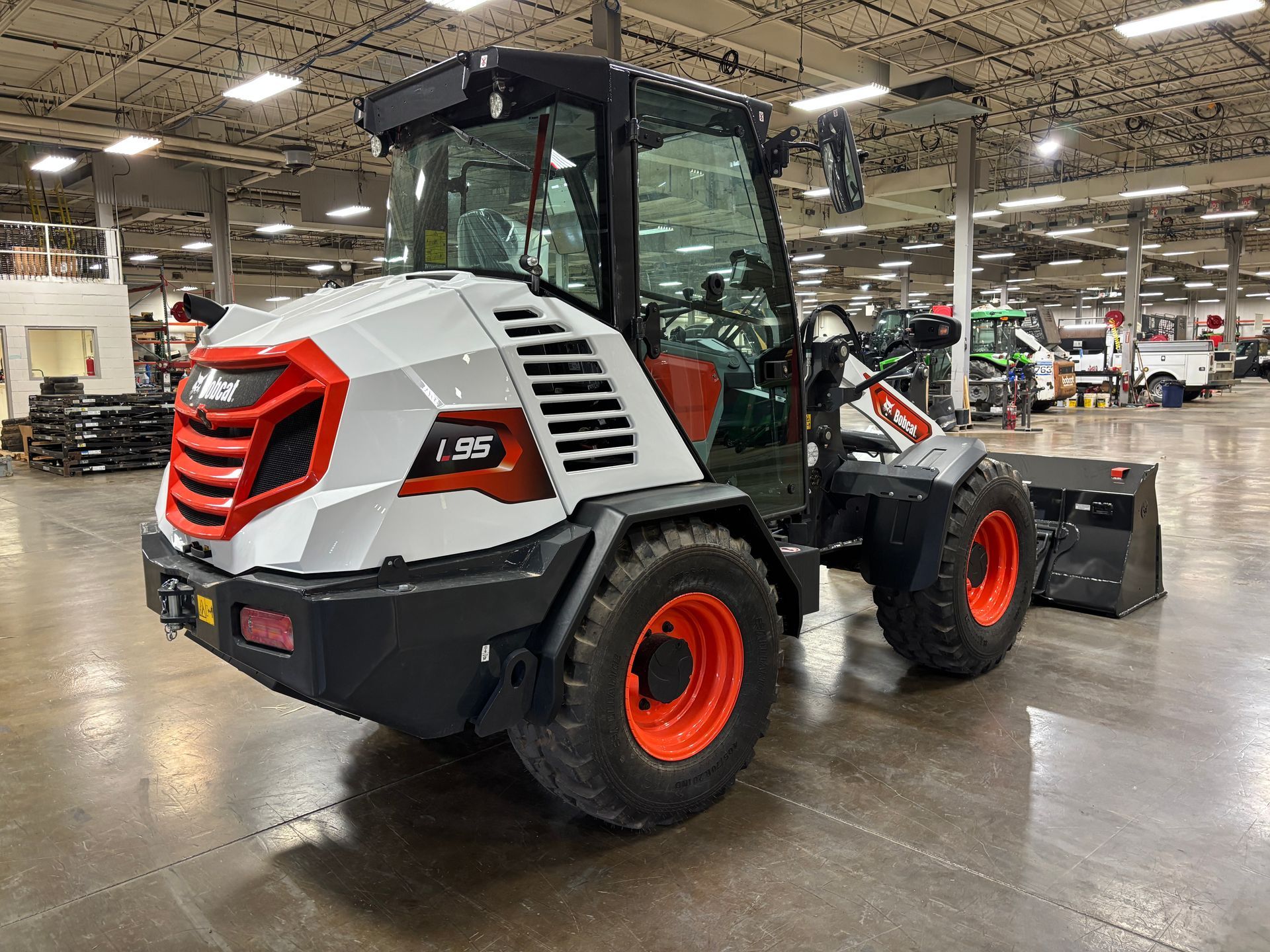 White and red Bobcat L95 compact wheel loader with orange wheels and a black cab in a warehouse.