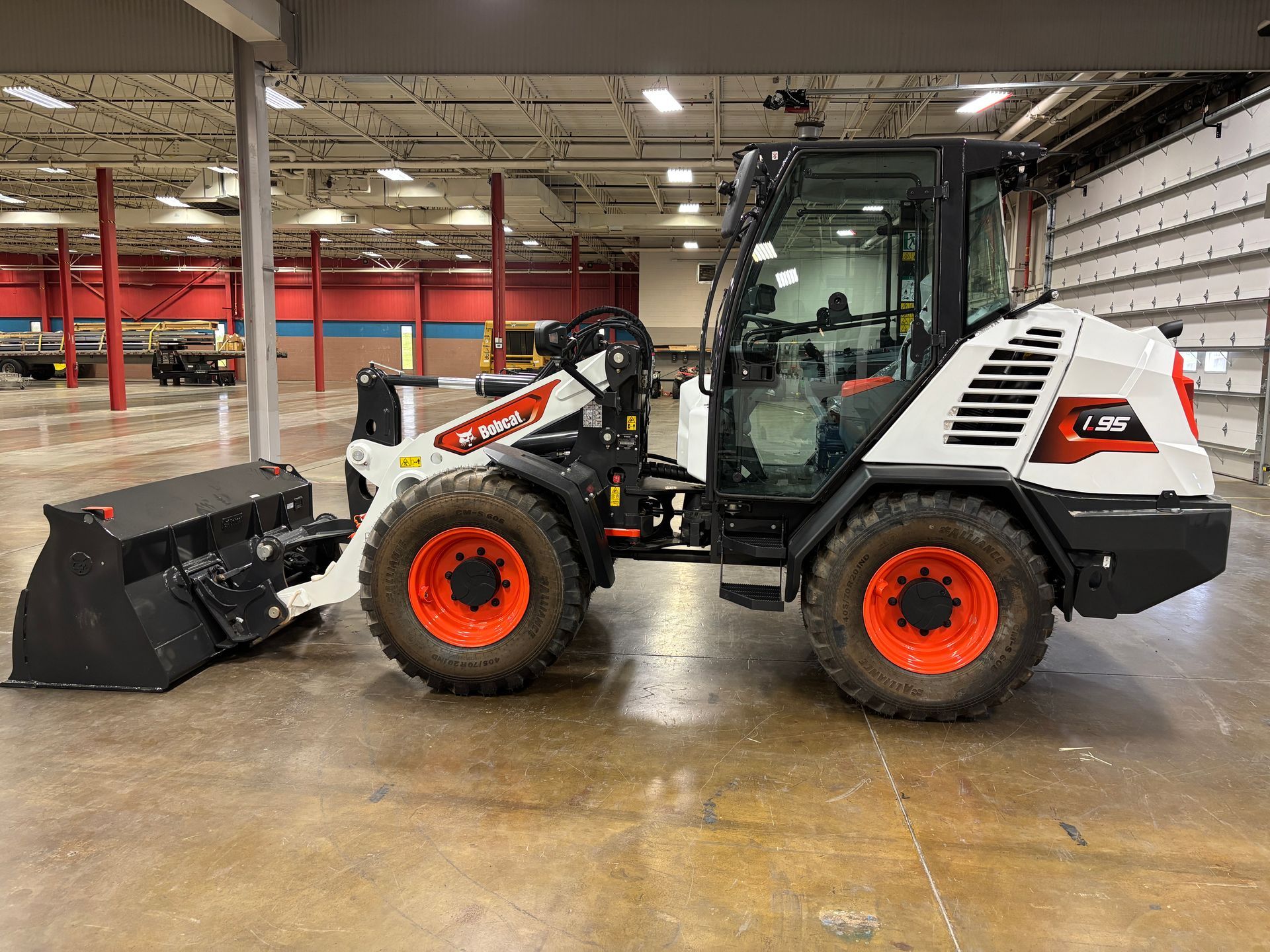White Bobcat compact wheel loader with orange wheels, bucket attached, indoors.