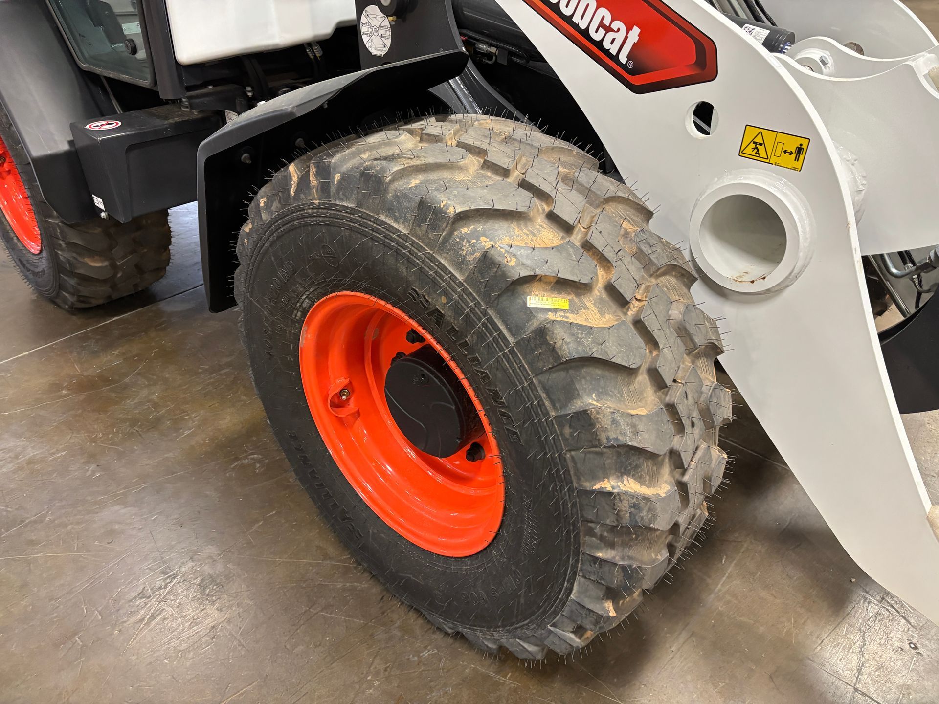 Close-up of a Bobcat skid-steer loader wheel with a rugged, black tire and a bright orange rim.