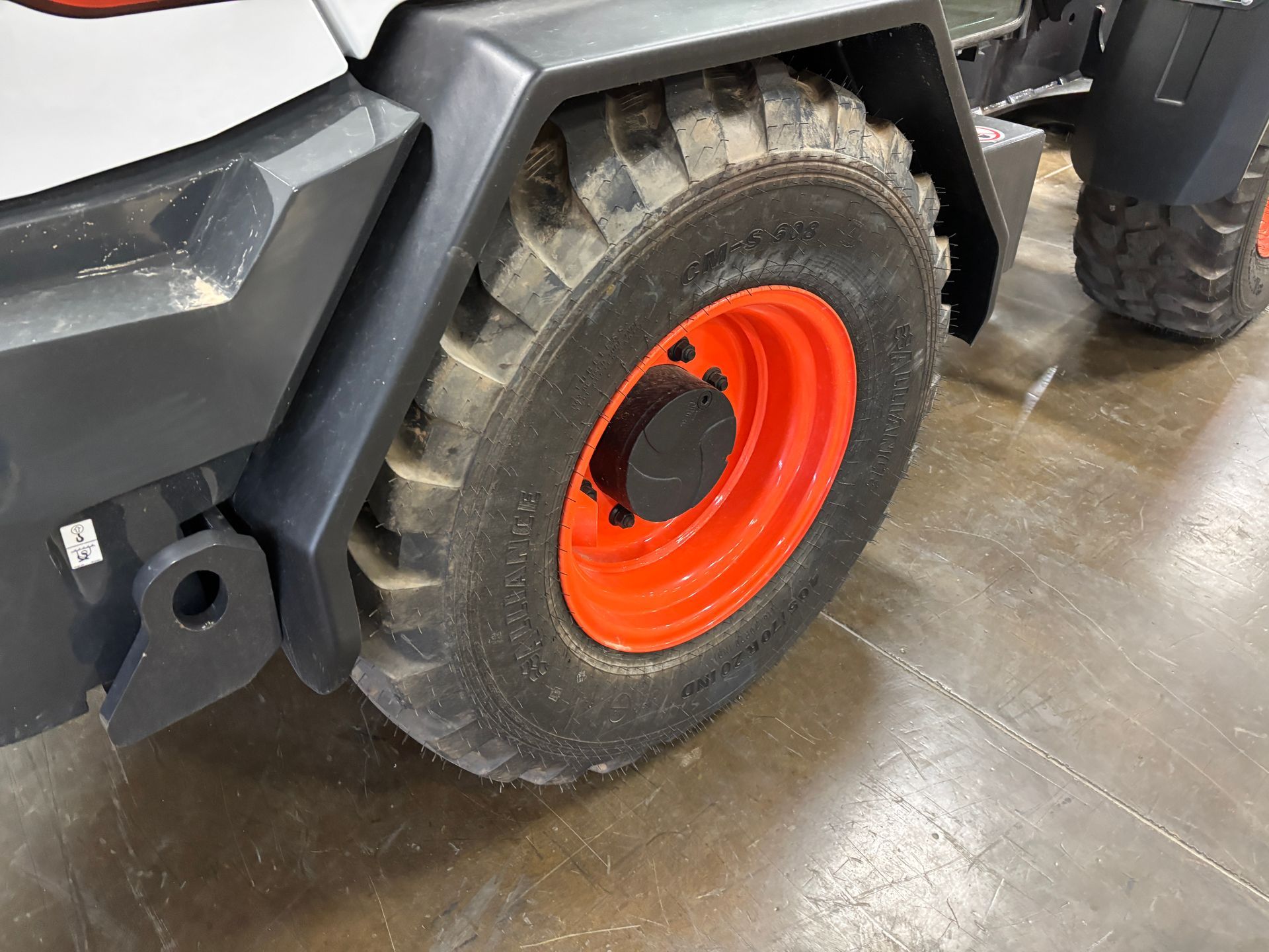 Close-up of a Bobcat wheel. The tire is black with an orange wheel rim, set on a gray floor.