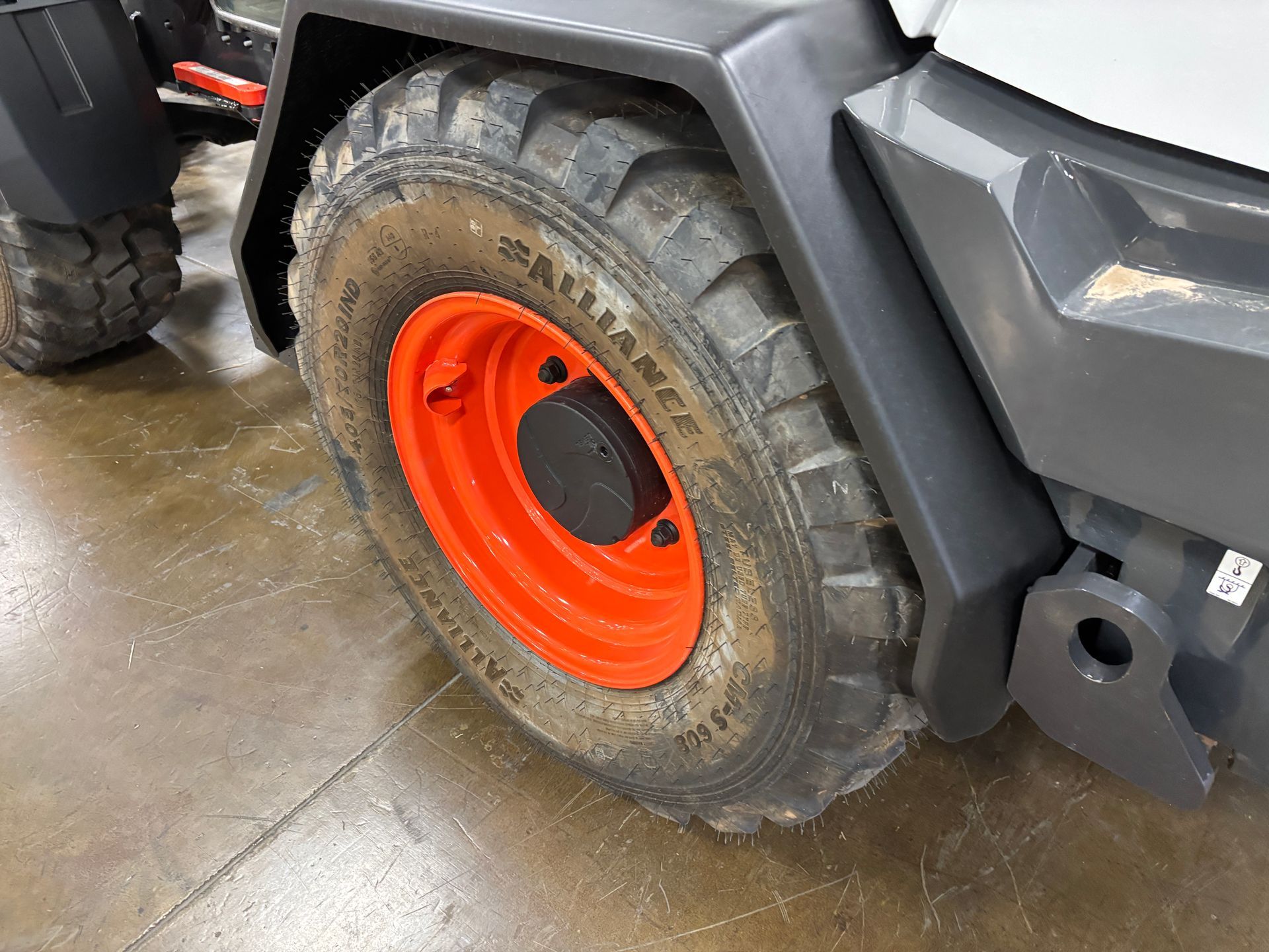 Close-up of a construction vehicle tire with an orange rim. The tire is dirty, and the setting appears indoors.