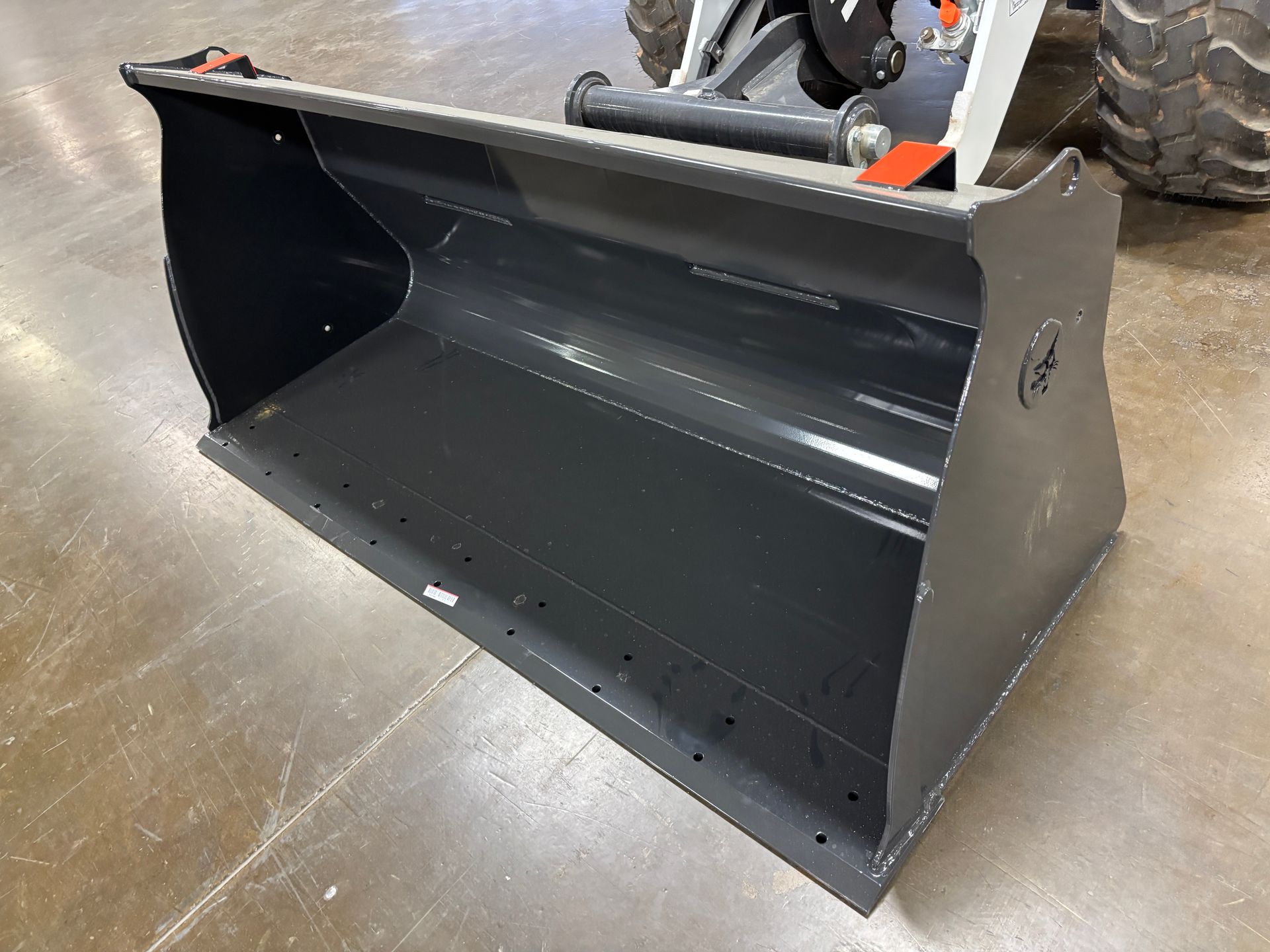 Gray metal bucket attachment for a loader, on a concrete floor.