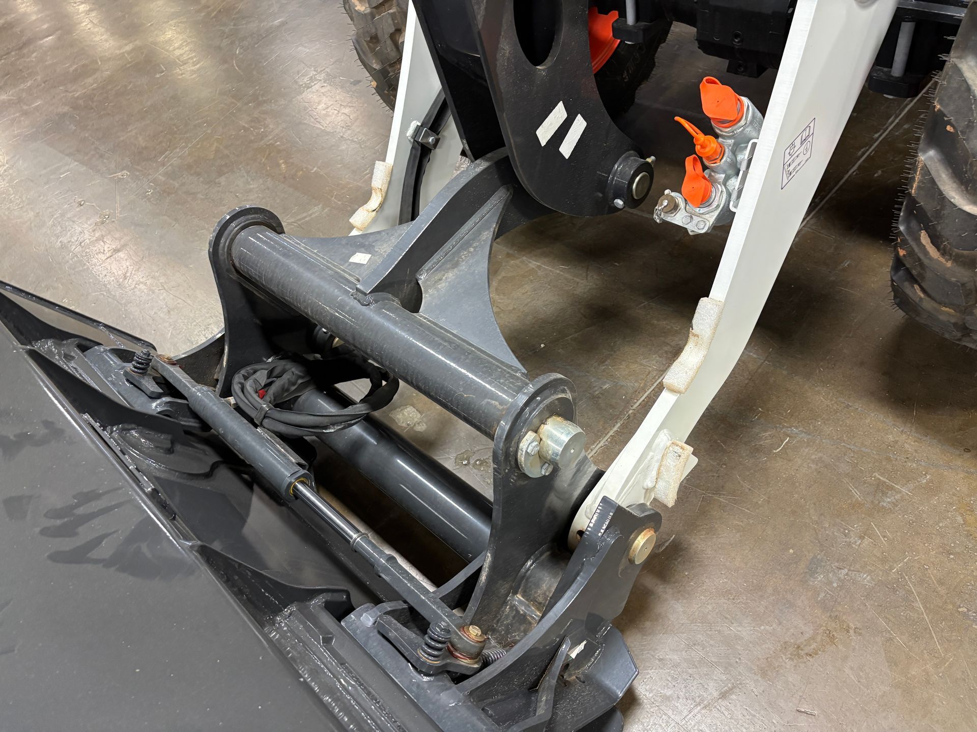 A close-up of a skid steer attachment with gray and white metal parts, showing bucket and lift mechanism.