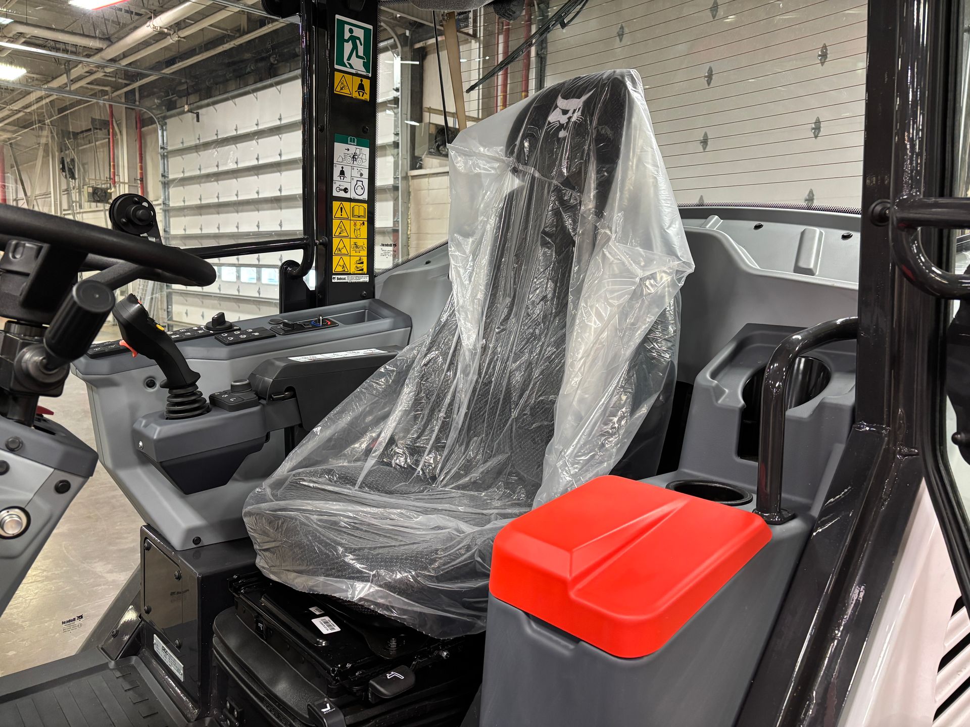 Bobcat tractor interior with plastic-covered seat and red armrest.