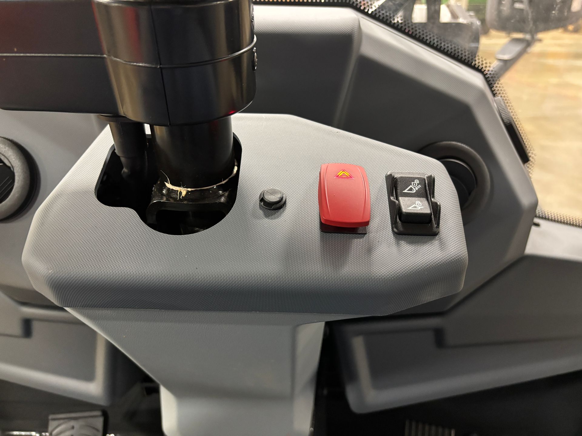 Control panel of a construction machine with buttons, joystick, and climate controls, angled view.