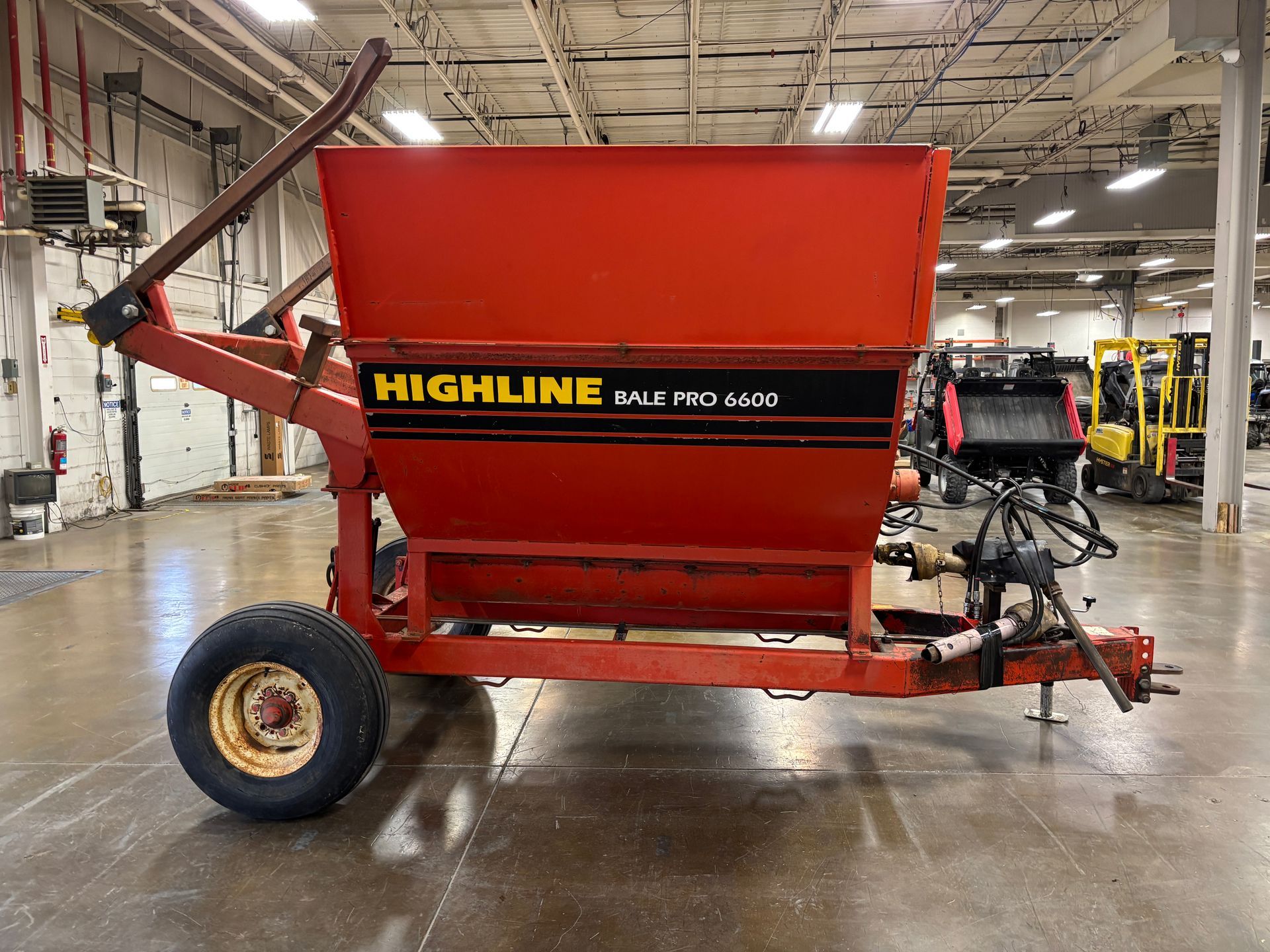 Red Highline bale processor on a trailer, in a warehouse, side view shot.