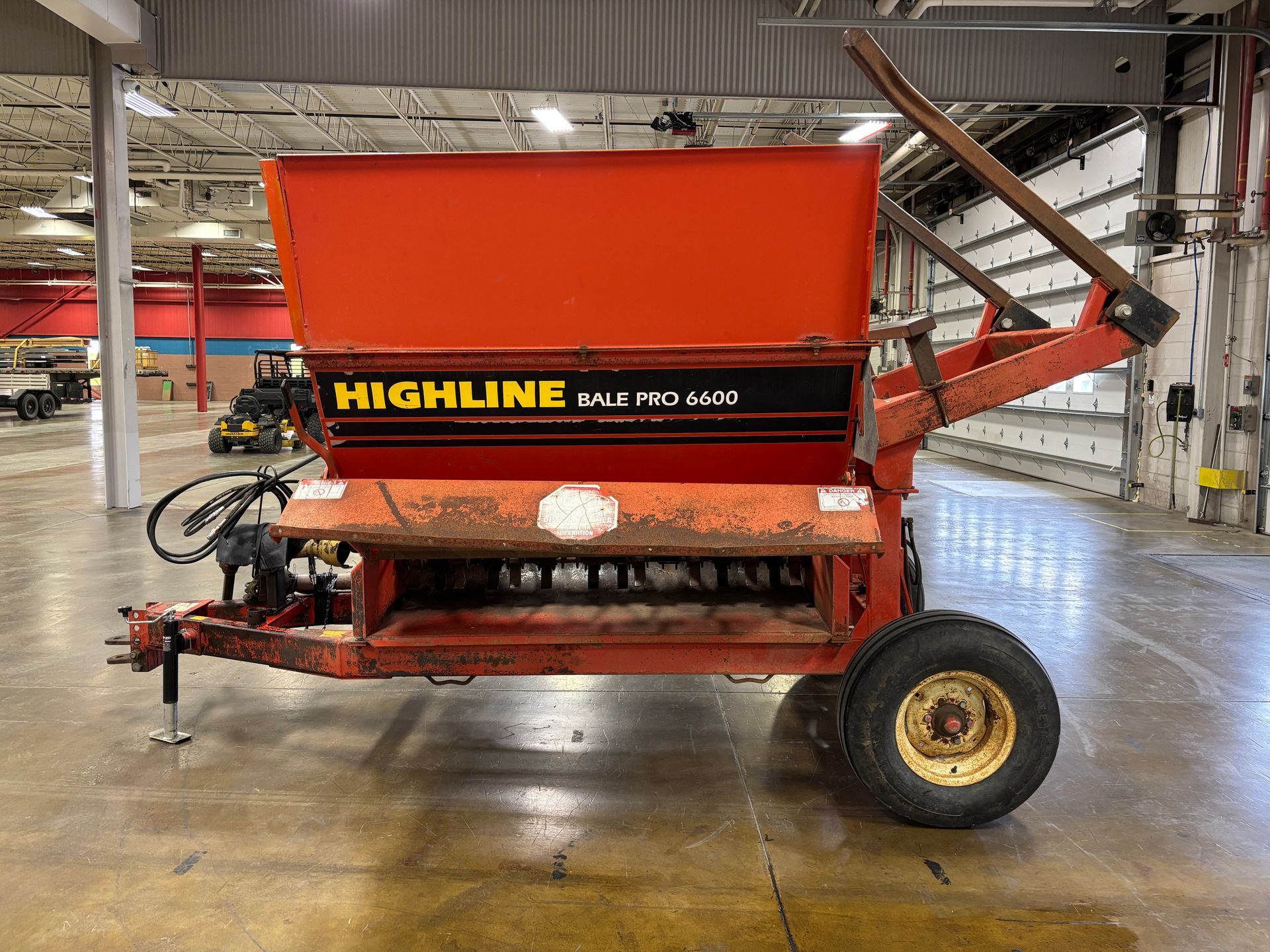 Red Highline bale processor on a trailer, in a warehouse, side view shot.