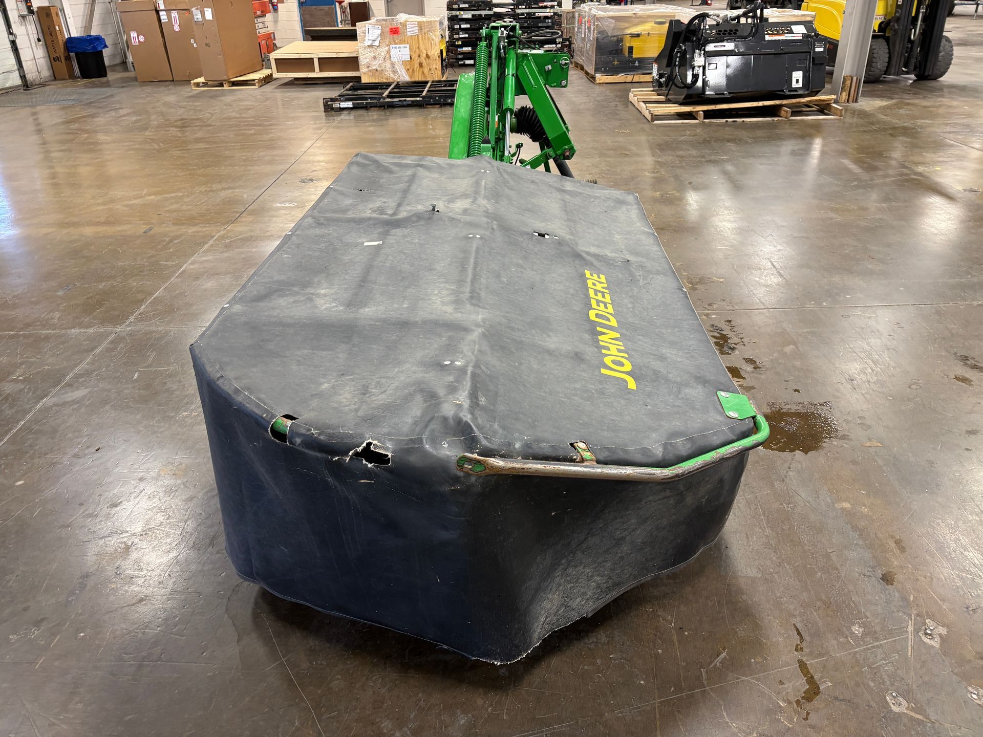 Green, covered John Deere disc mower on a concrete floor in a warehouse setting, back shot.