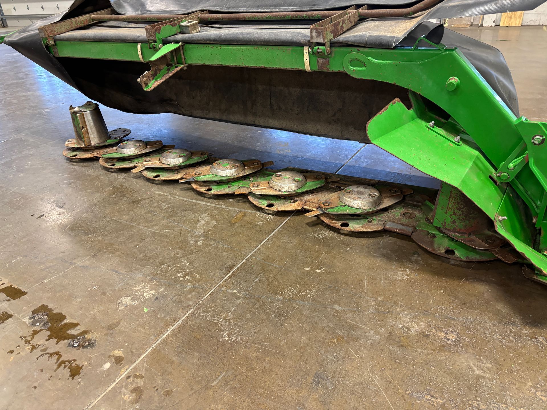 Green farm mower blades resting on a concrete floor, angled shot.