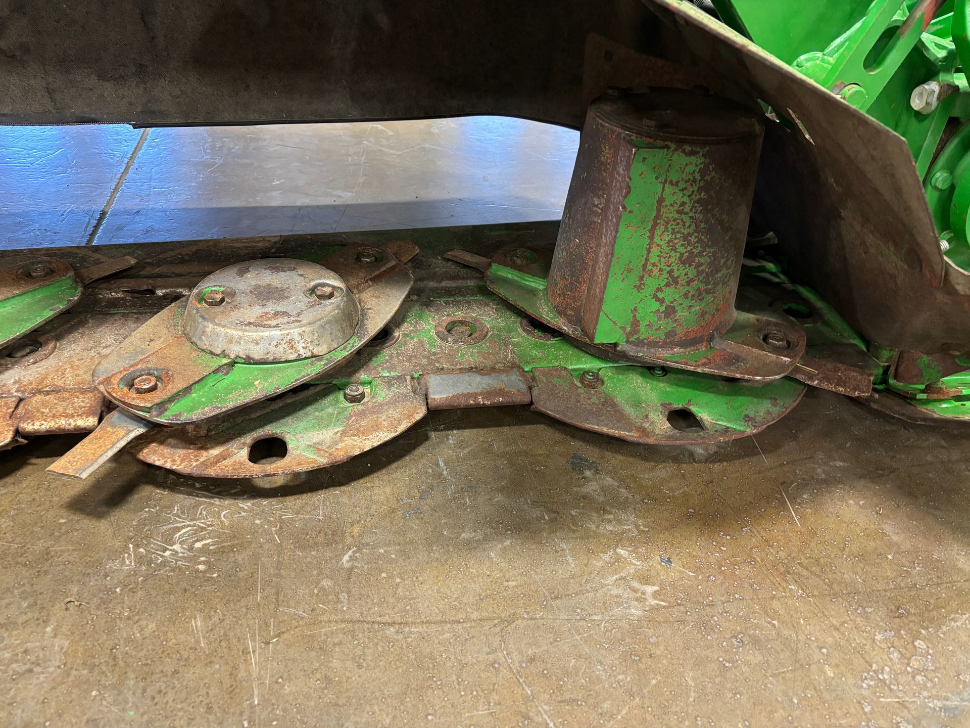 Green farm mower blades resting on a concrete floor, closeup shot.