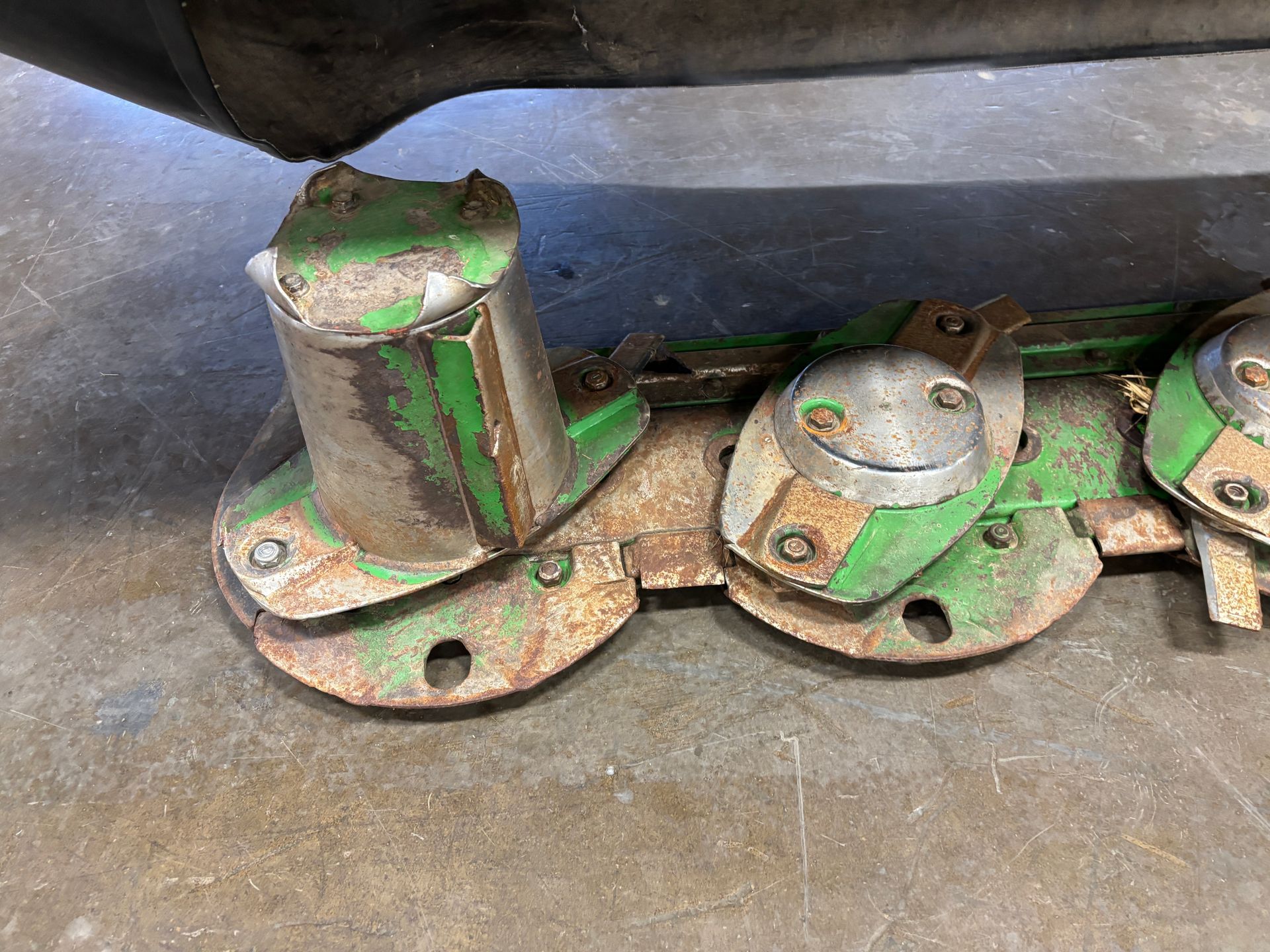 Green farm mower blades resting on a concrete floor, closeup shot.