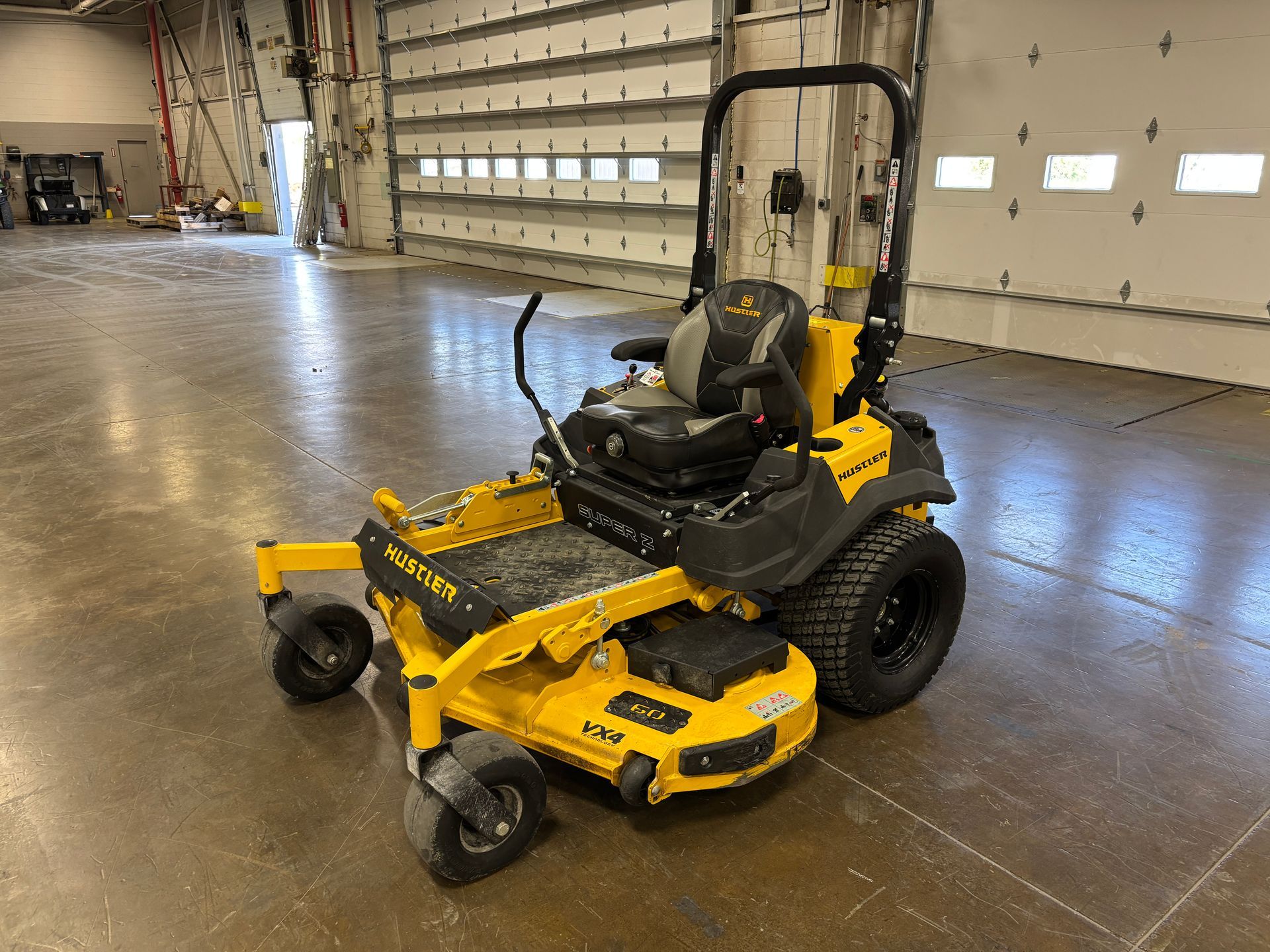 Yellow zero-turn lawn mower in a garage with a roll-up door.