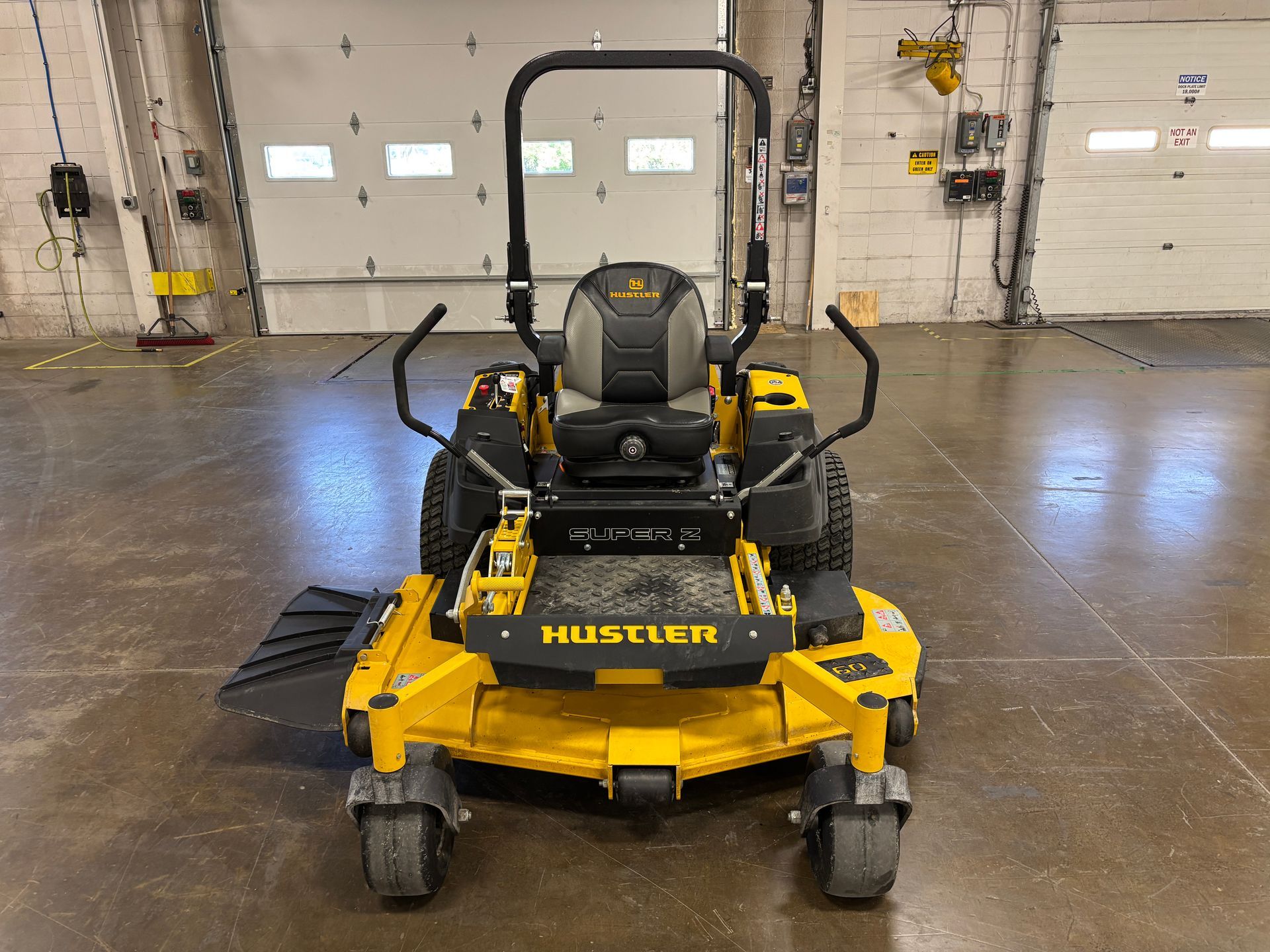 Yellow Hustler zero-turn mower, front view, in a warehouse setting.