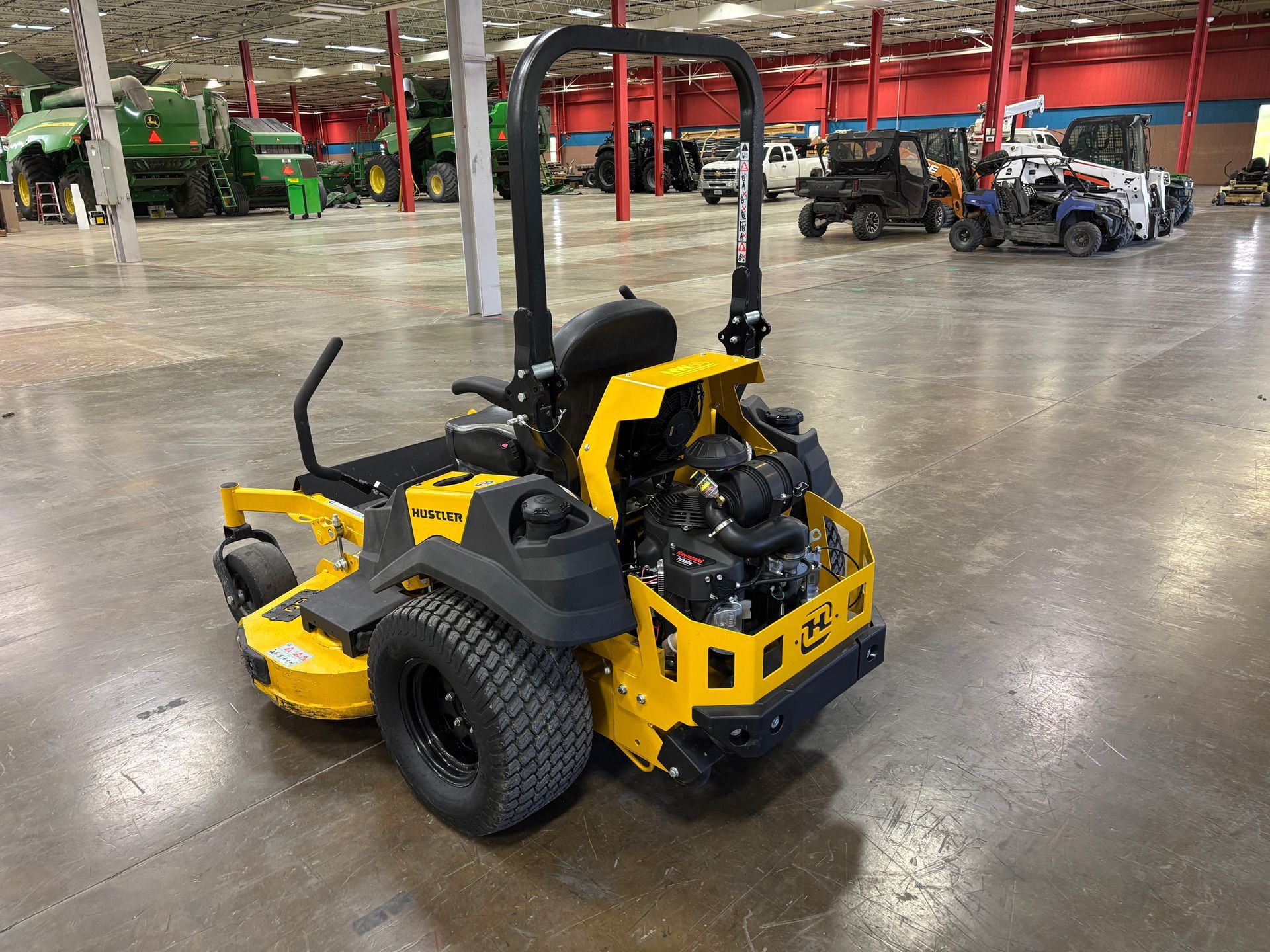 Yellow zero-turn lawnmower on a gray concrete floor inside a large warehouse.