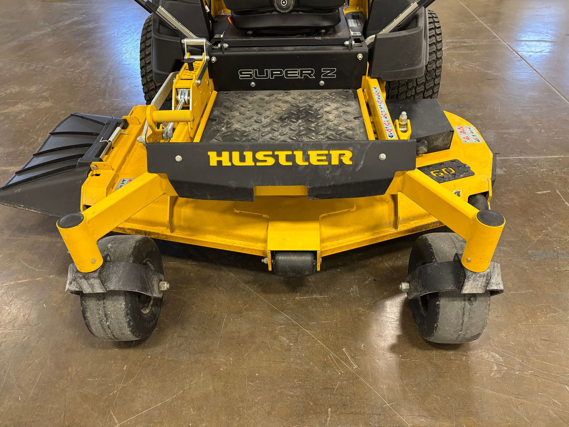 Yellow Hustler zero-turn mower, front view, black accents, on a concrete floor.