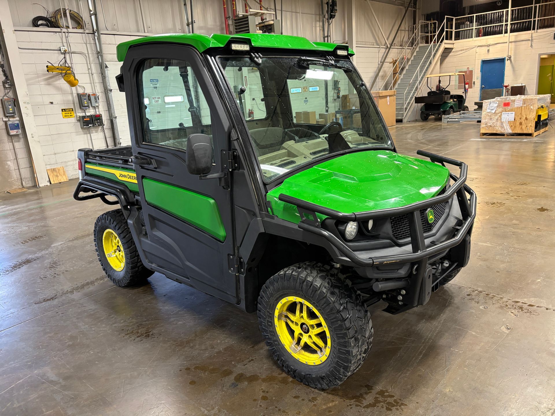 John Deere Gator utility vehicle with green and yellow accents. Inside a building.