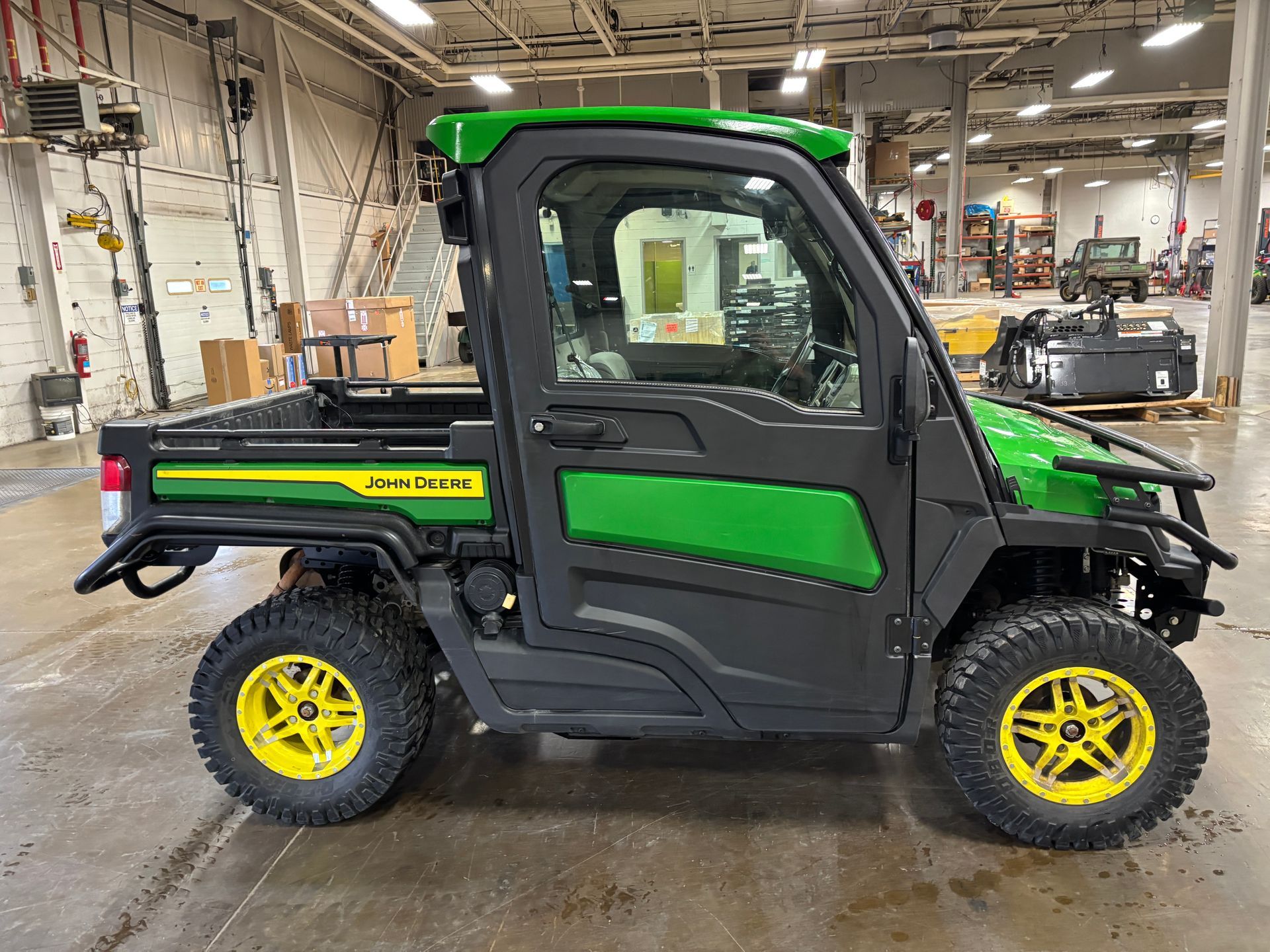 John Deere Gator utility vehicle, green and black, with yellow wheels, indoors.
