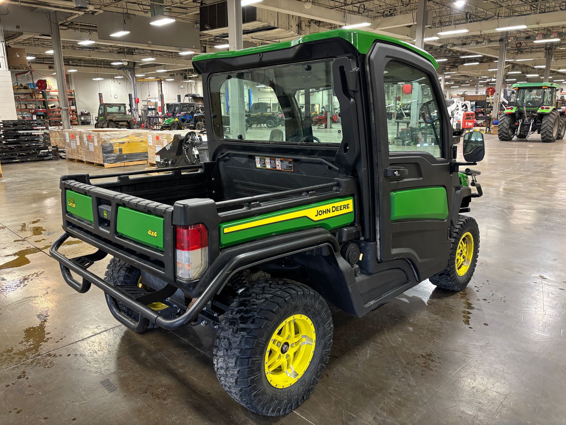 Green and black John Deere Gator utility vehicle with a covered cab, on an indoor floor.
