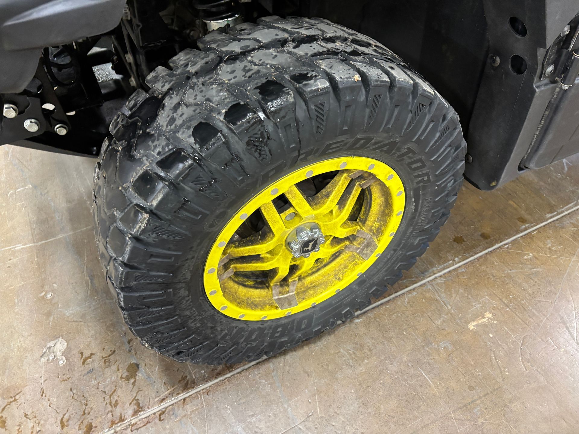 Off-road vehicle tire with deep tread, mounted on a yellow wheel, on a concrete surface.