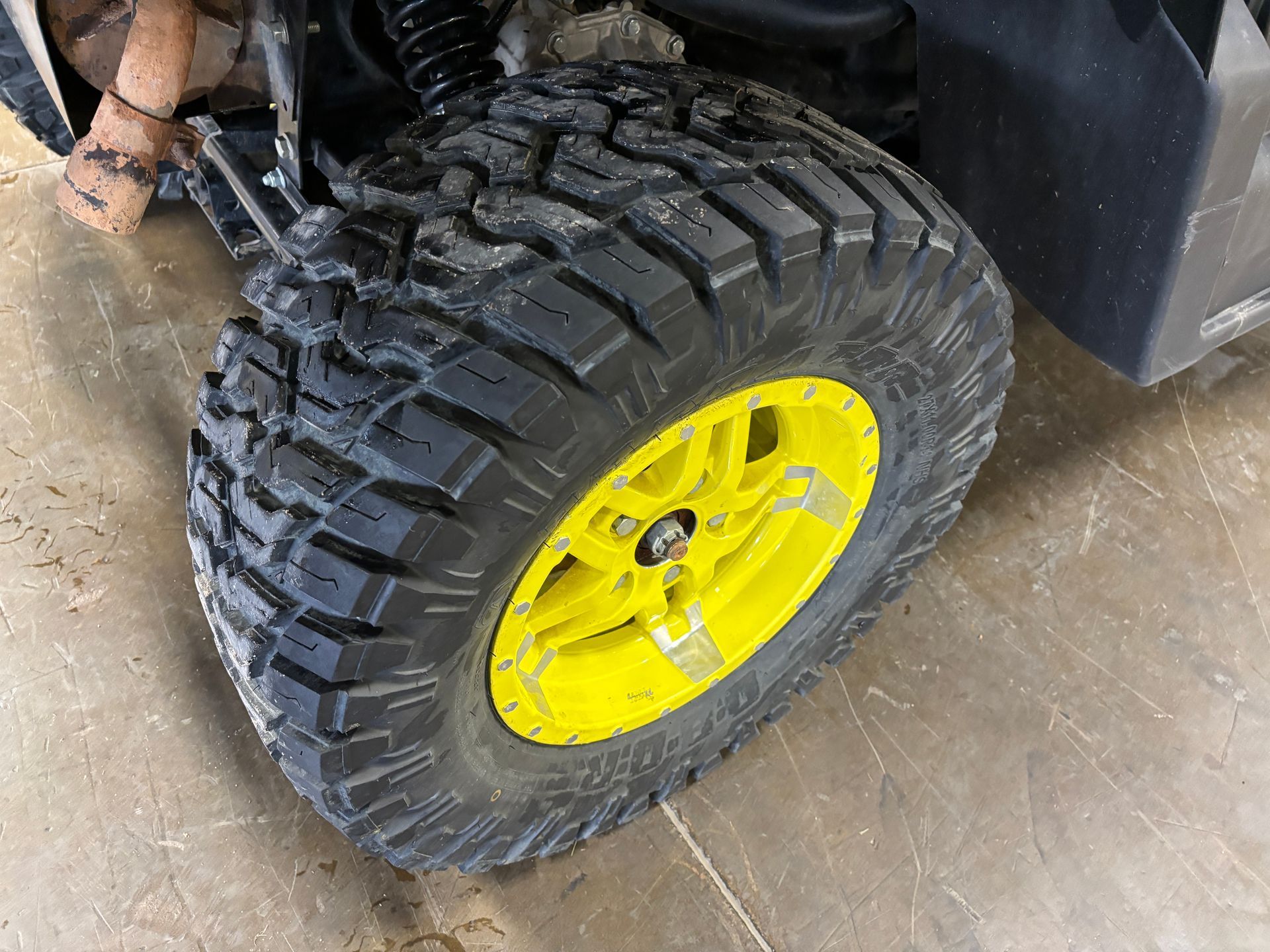 Off-road vehicle tire with black tread and a bright yellow rim, on a gray concrete floor.