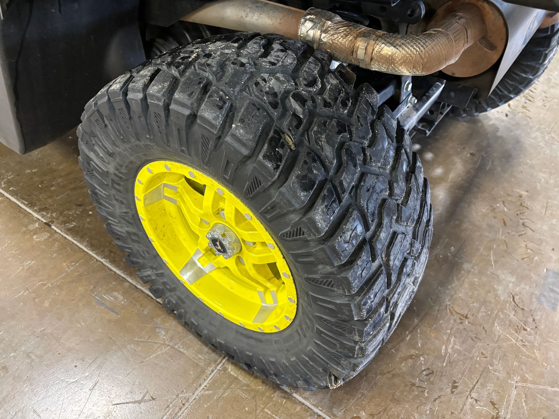 Yellow off-road wheel and tire on a vehicle, showing tread and exhaust pipe.