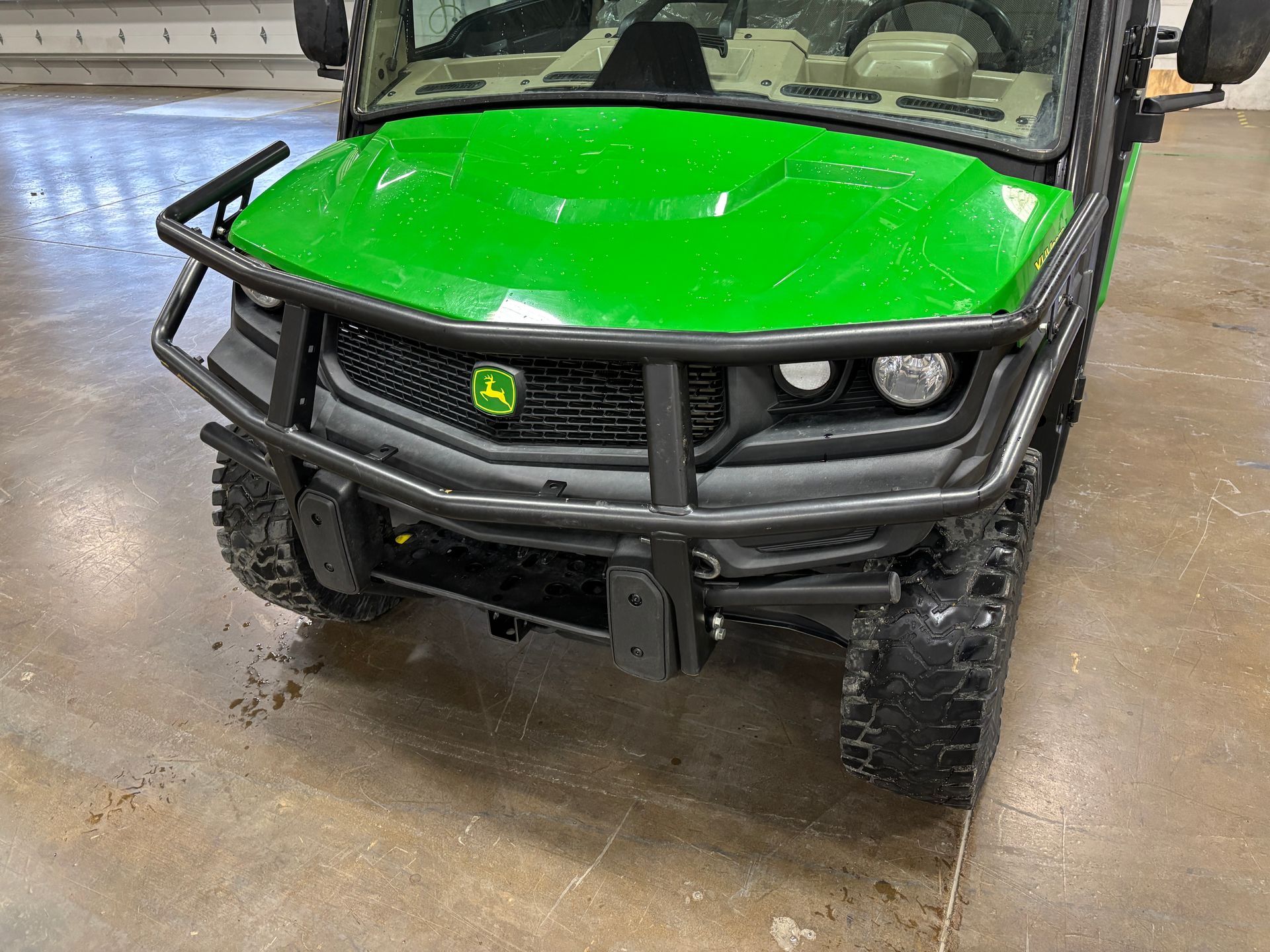 Green and black John Deere Gator utility vehicle with a front bumper, on a concrete surface.