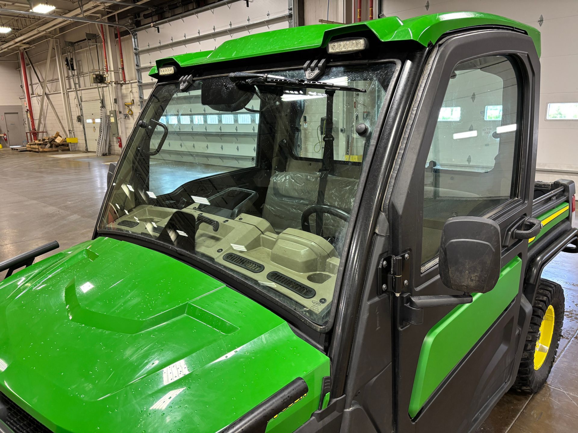 Green John Deere Gator UTV with windshield, lights, and cab.