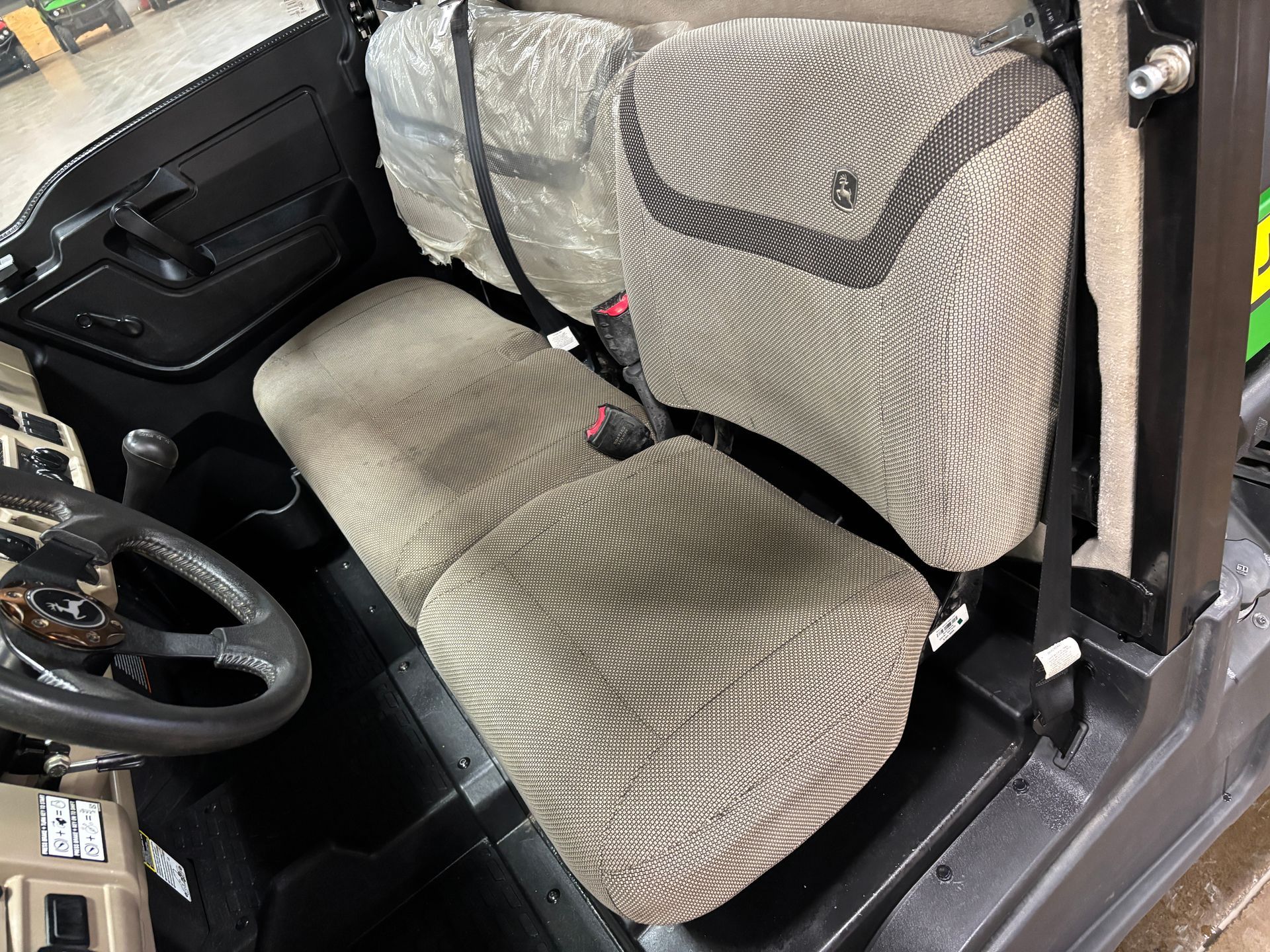 Interior of a side-by-side vehicle with two seats, neutral-toned fabric, black frame, and steering wheel.