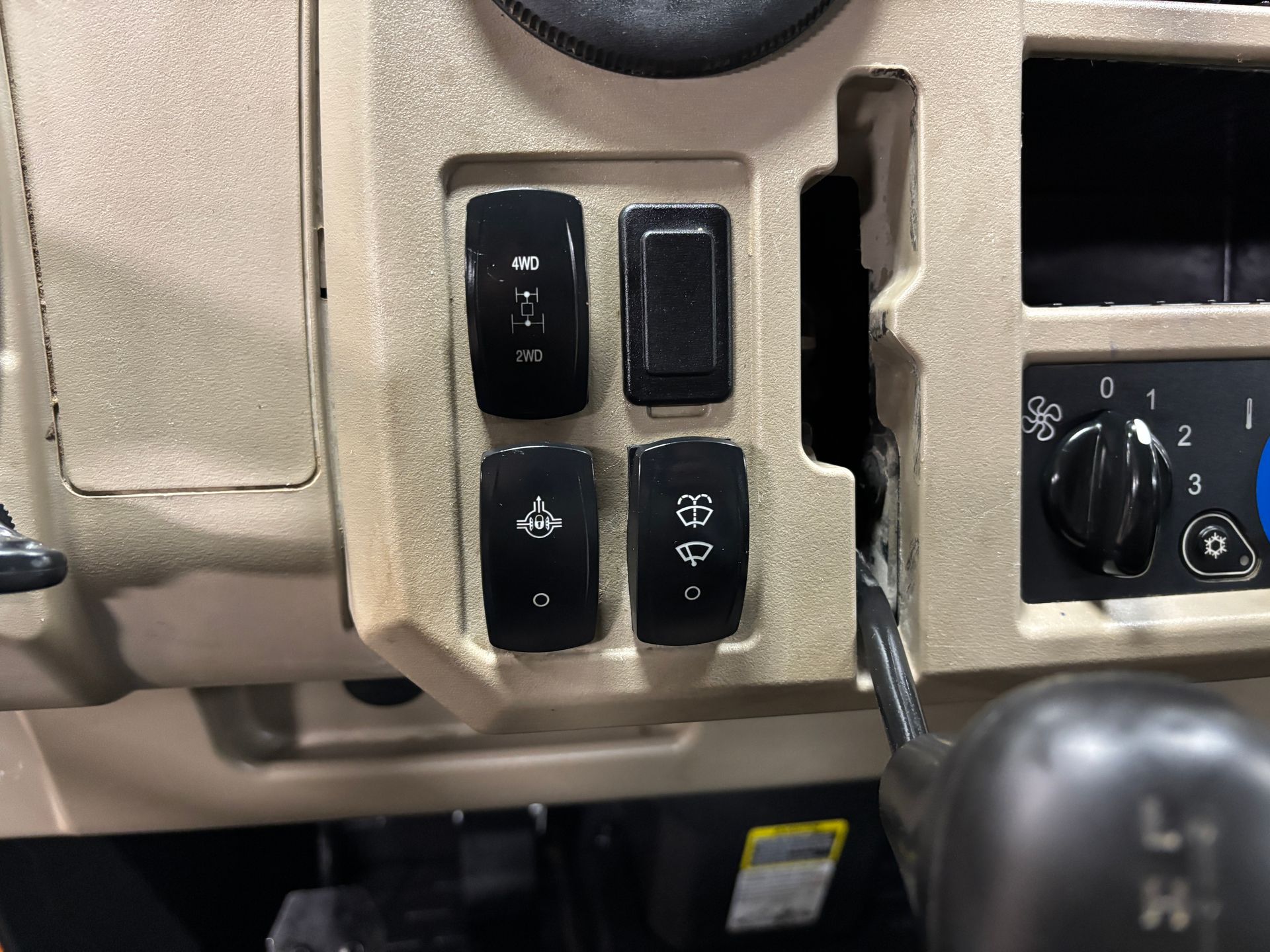 Close-up of a vehicle dashboard with four black switches. Beige interior and a gear shift.