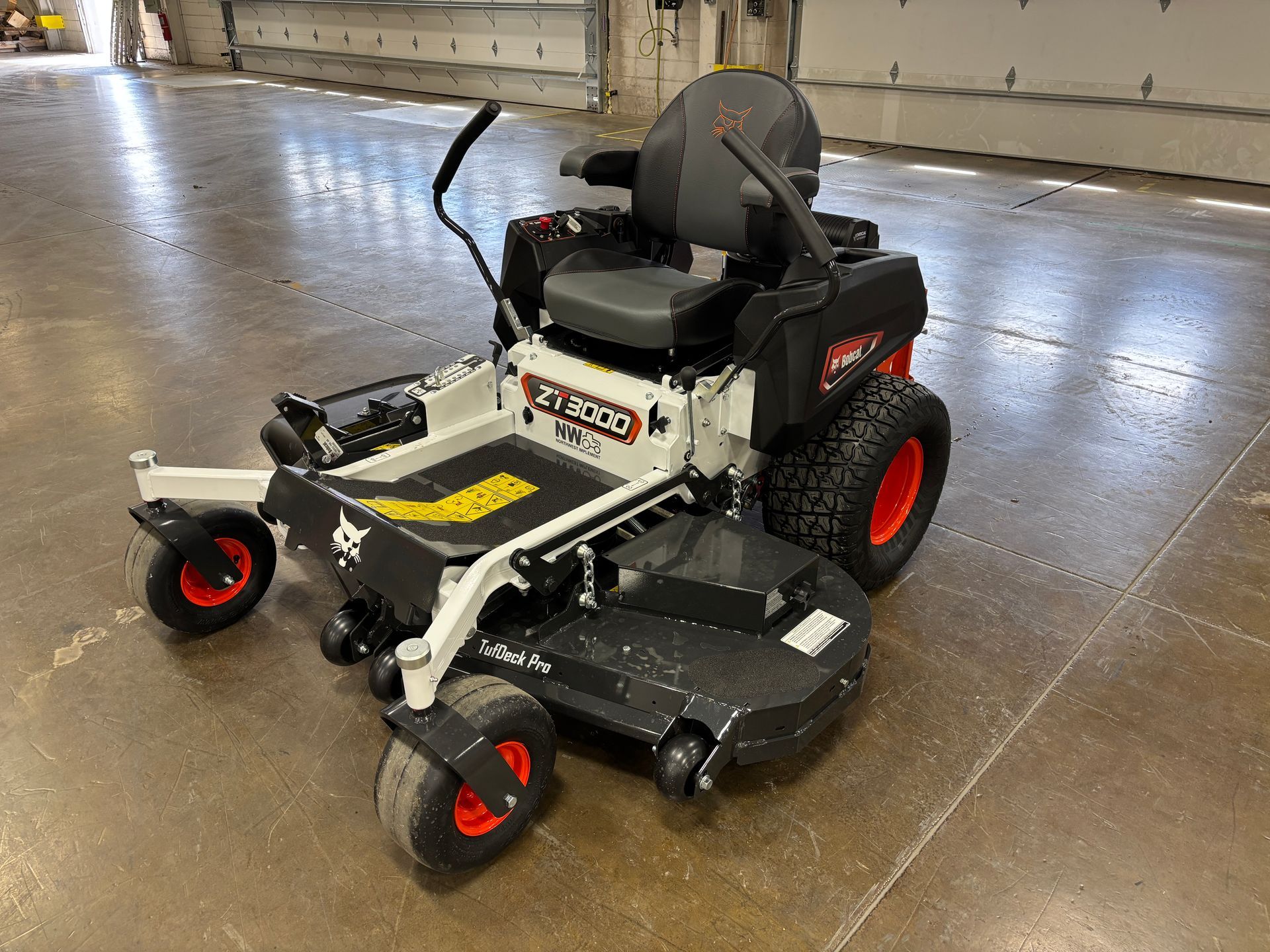 White and black Bobcat zero-turn mower with orange wheels, indoors.
