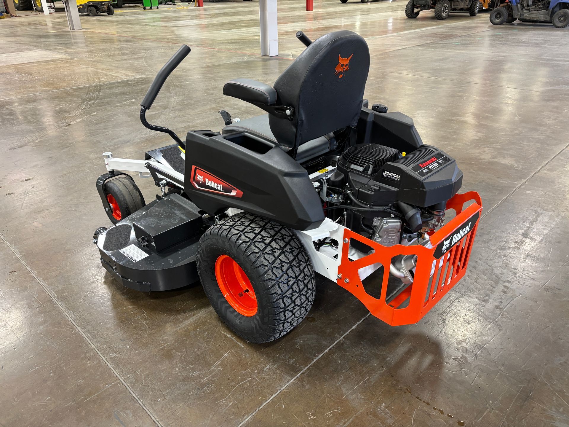 Bobcat zero-turn lawn mower on a concrete floor. It is black, white, and orange, and the wheels have large treads.