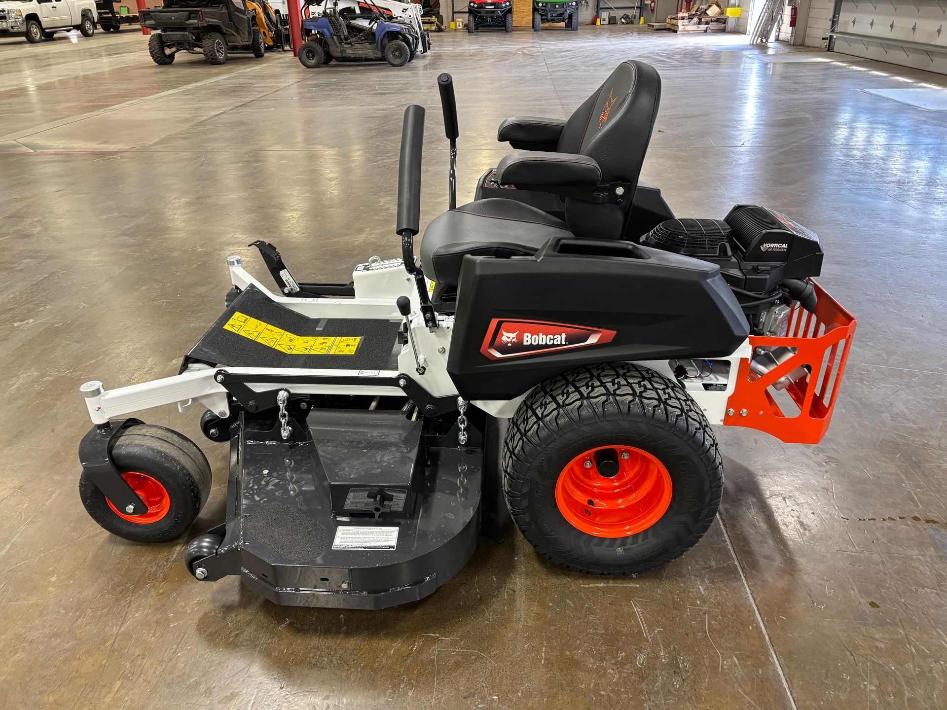 White and black Bobcat zero-turn mower with orange accents on the wheels and rear cage; indoors.