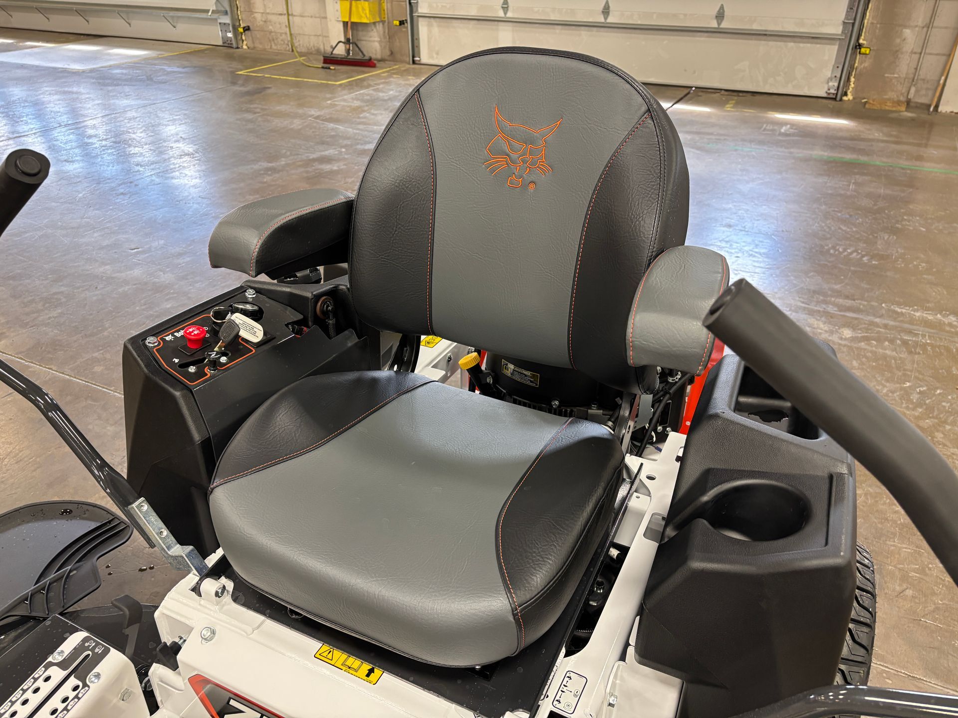 Bobcat zero-turn mower seat. Gray and black cushioned seat with armrests, cup holder, and control panel.