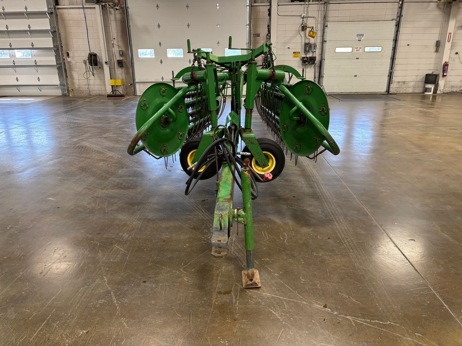 John Deere hay rake, green, on a concrete floor in a warehouse.